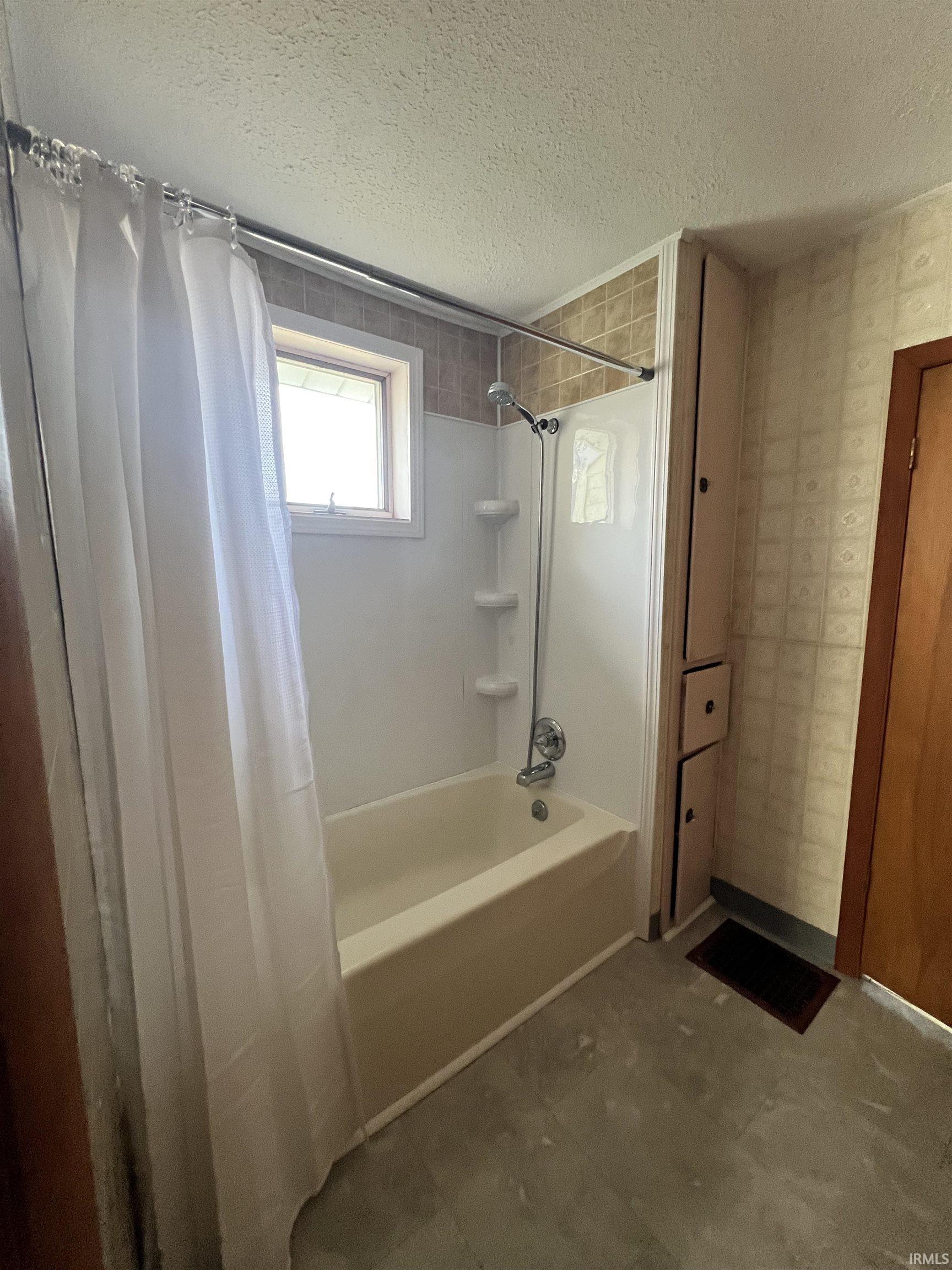 Bathroom featuring shower / bathtub combination with curtain, wallpapered walls, and a textured ceiling