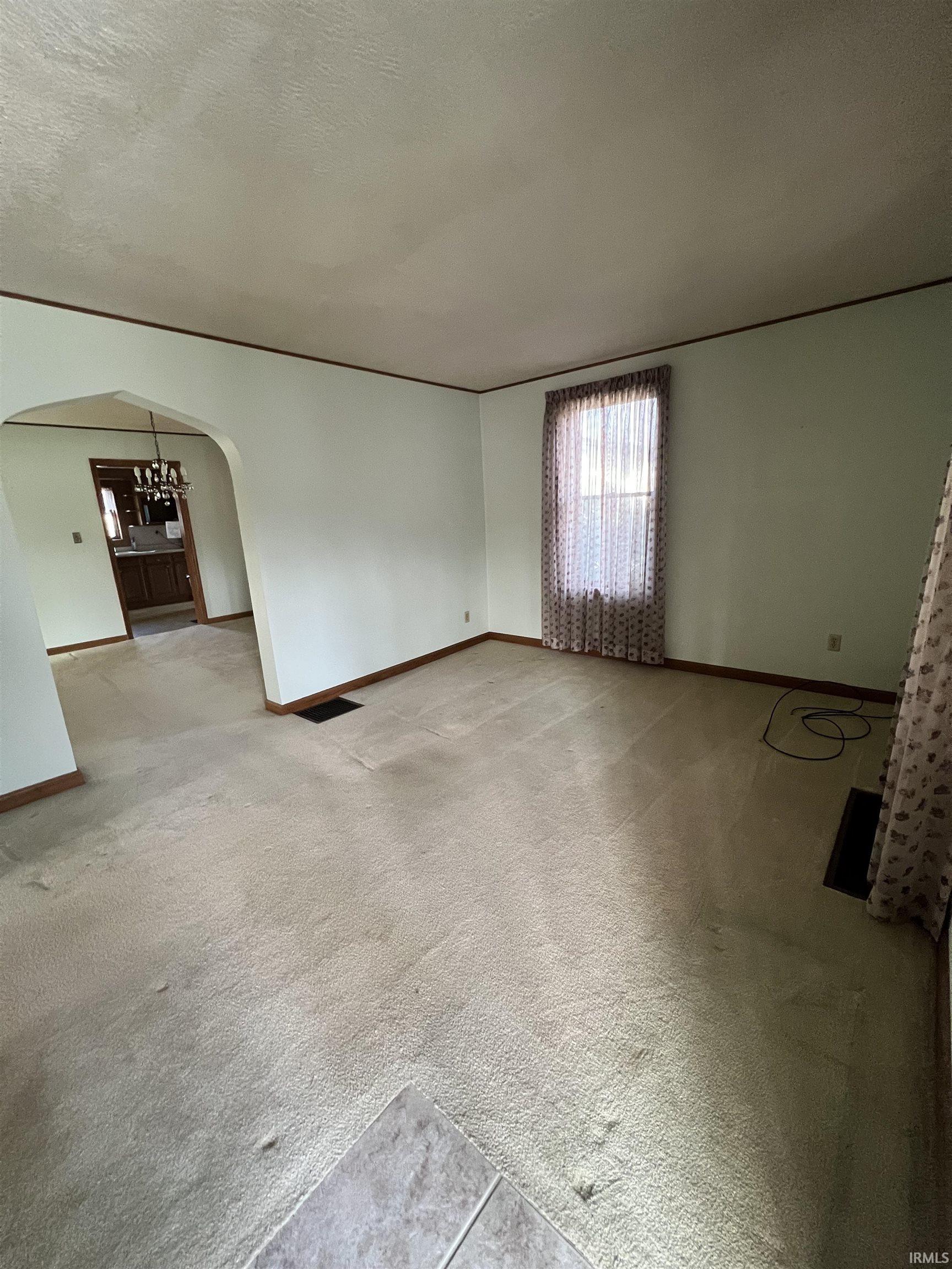 Carpeted spare room featuring a textured ceiling and arched walkways