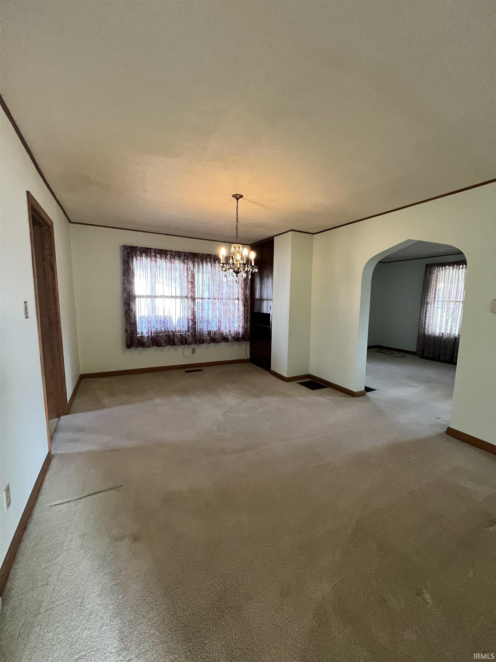 Unfurnished dining area with arched walkways, a chandelier, light carpet, and plenty of natural light