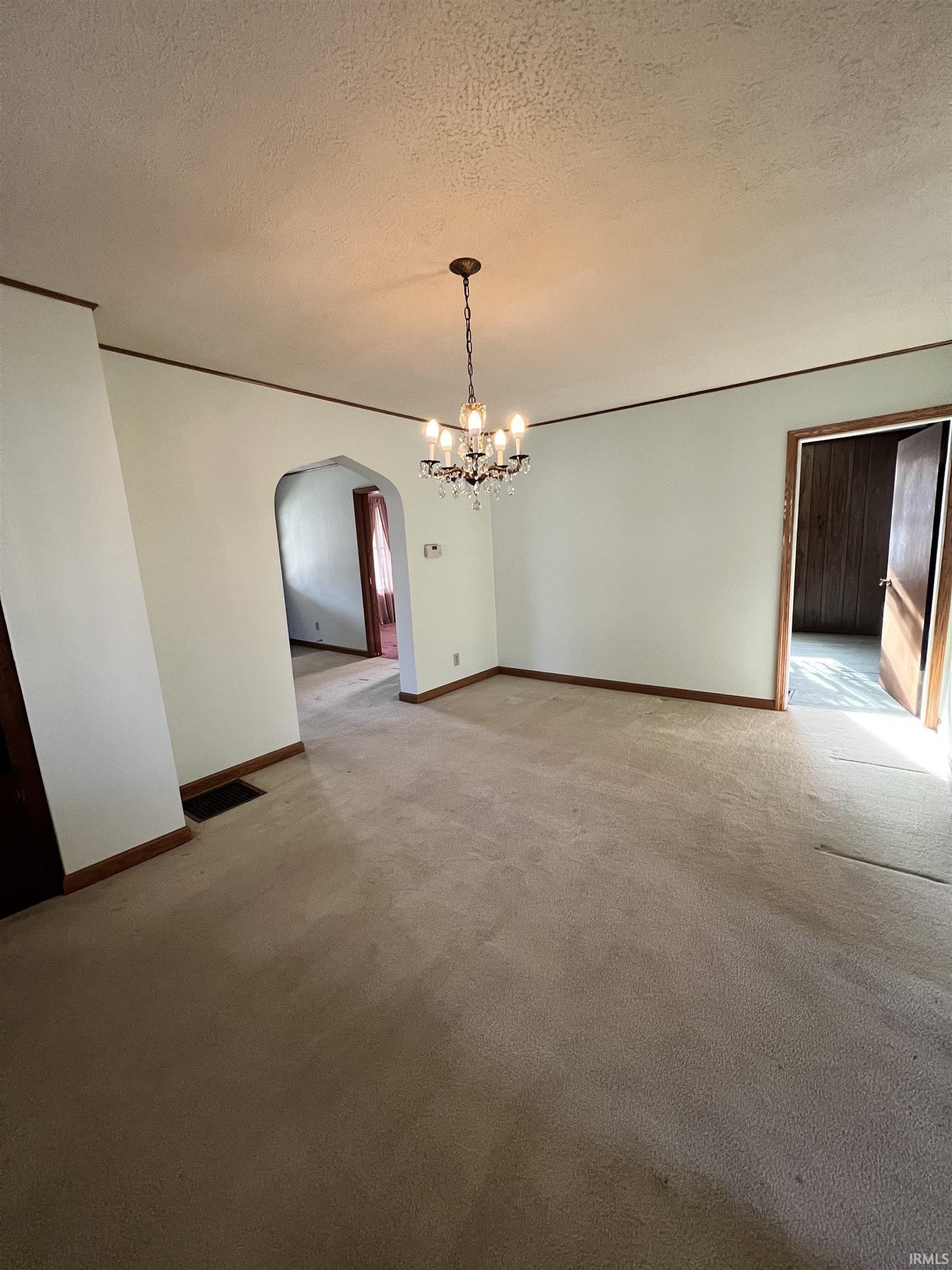 Unfurnished dining area featuring arched walkways, a textured ceiling, a chandelier, and light colored carpet