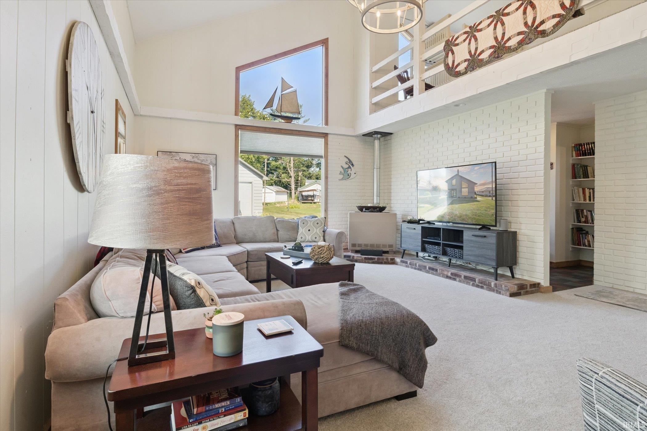 Living area featuring a towering ceiling, carpet flooring, and brick wall