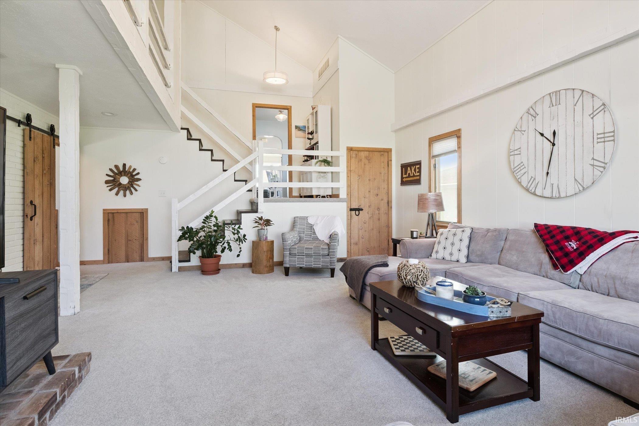 Carpeted living room with a barn door, stairway, and high vaulted ceiling