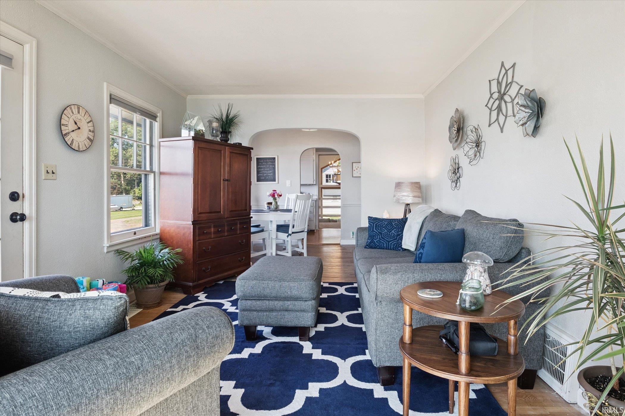 Living room with arched walkways, wood finished floors, and ornamental molding