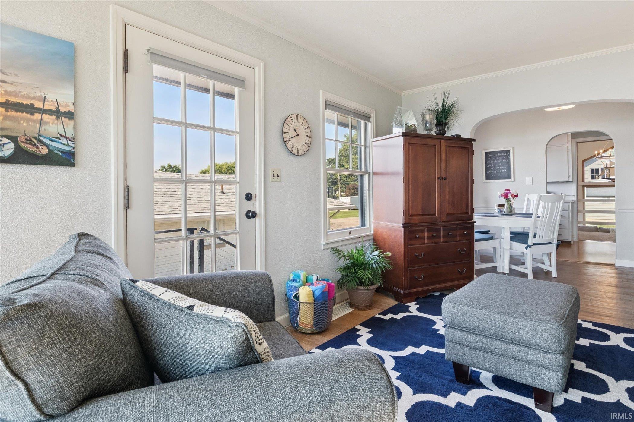Living area with arched walkways, wood finished floors, and ornamental molding