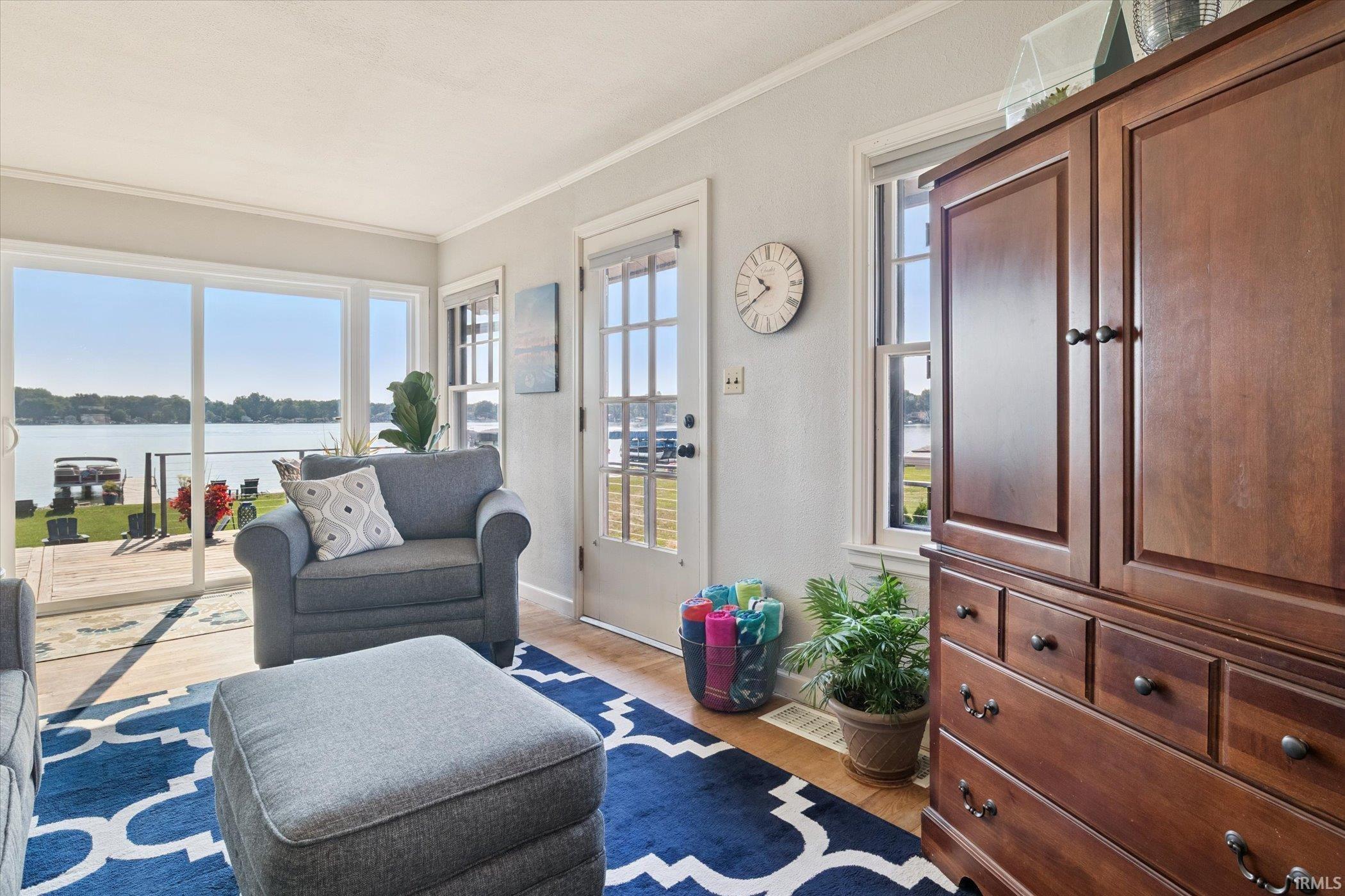 Living room with a water view, ornamental molding, and light wood-style flooring