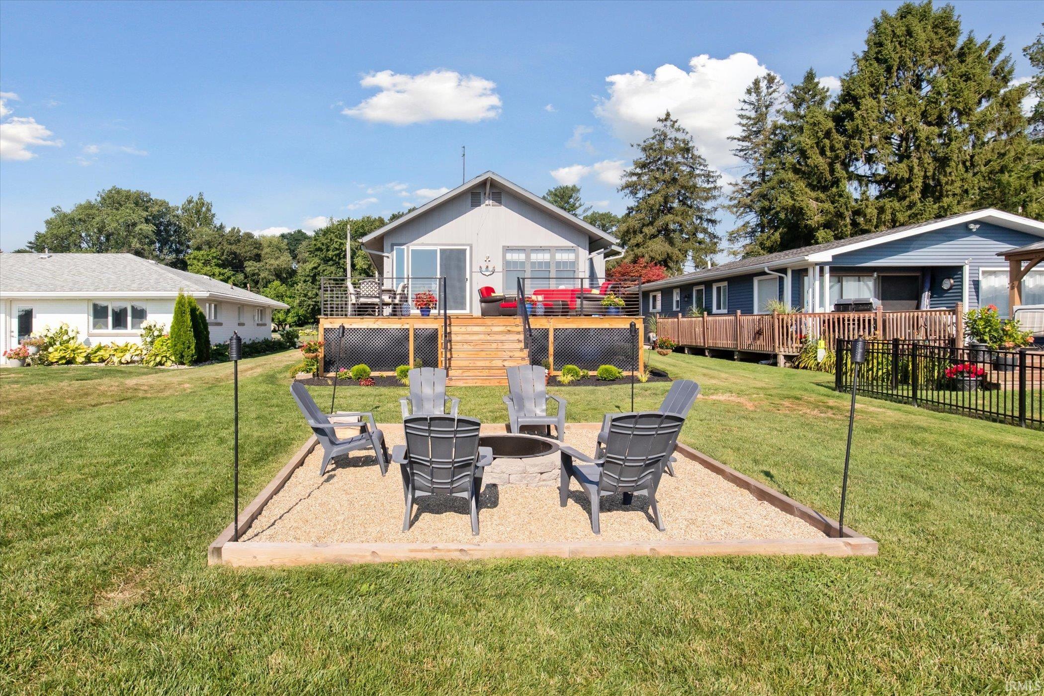 View of green lawn featuring a fire pit, a patio, and a wooden deck