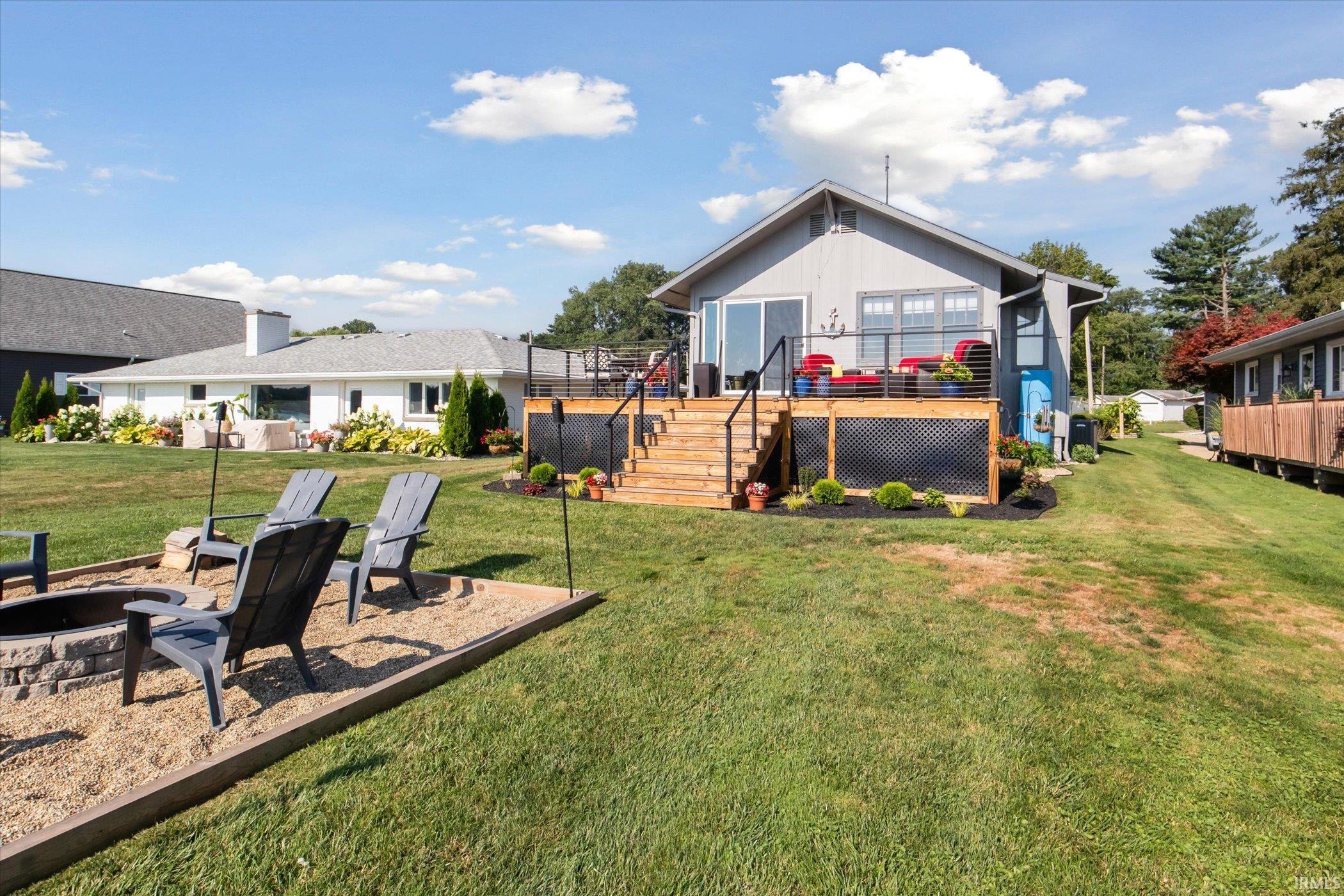 Rear view of property featuring an outdoor fire pit, a wooden deck, a lawn, stairs, and a patio