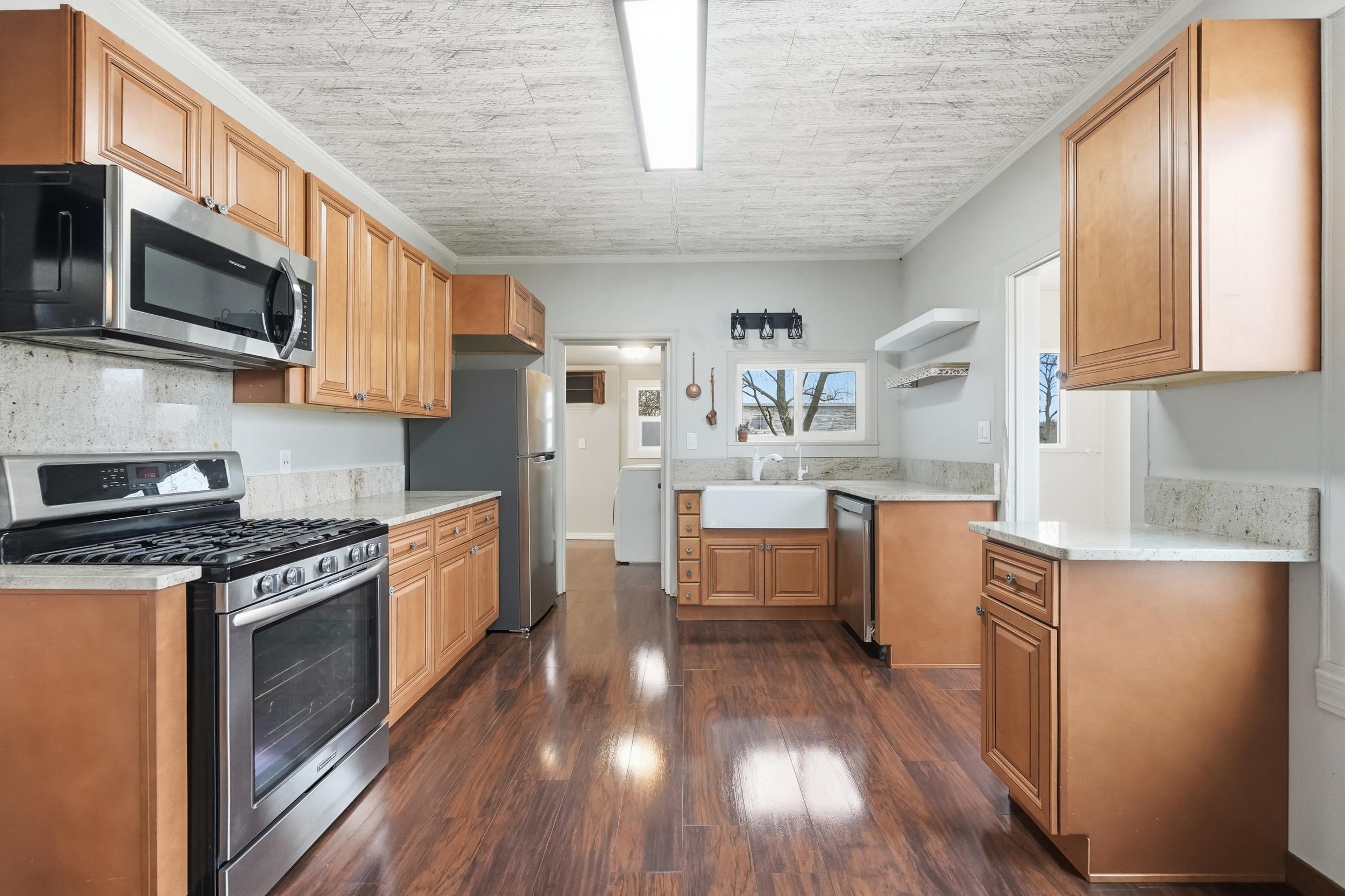 Kitchen featuring appliances with stainless steel finishes, dark wood-style flooring, open shelves, light stone countertops, and brown cabinets