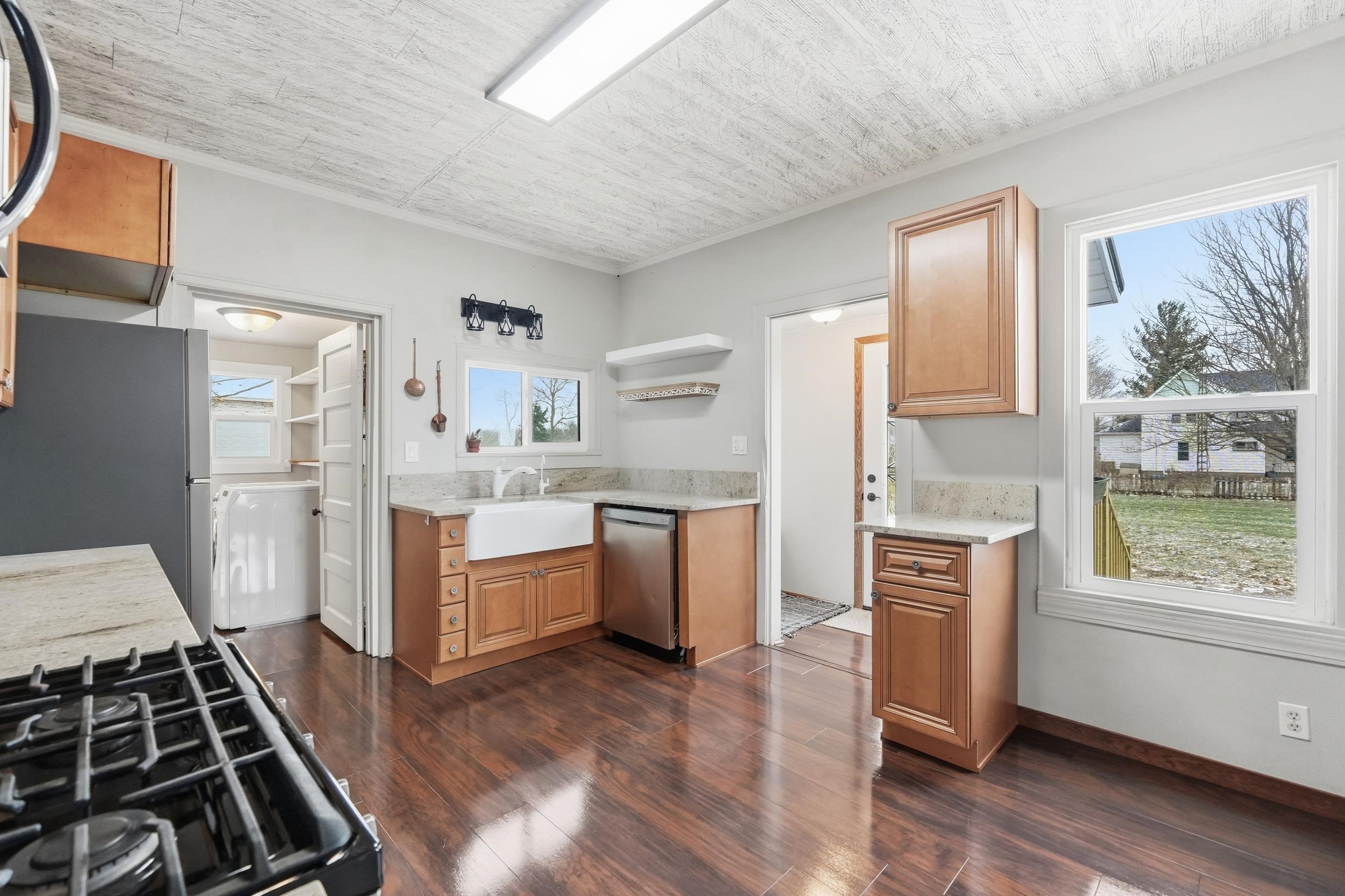 Kitchen featuring open shelves, appliances with stainless steel finishes, dark wood finished floors, light stone counters, and ornamental molding
