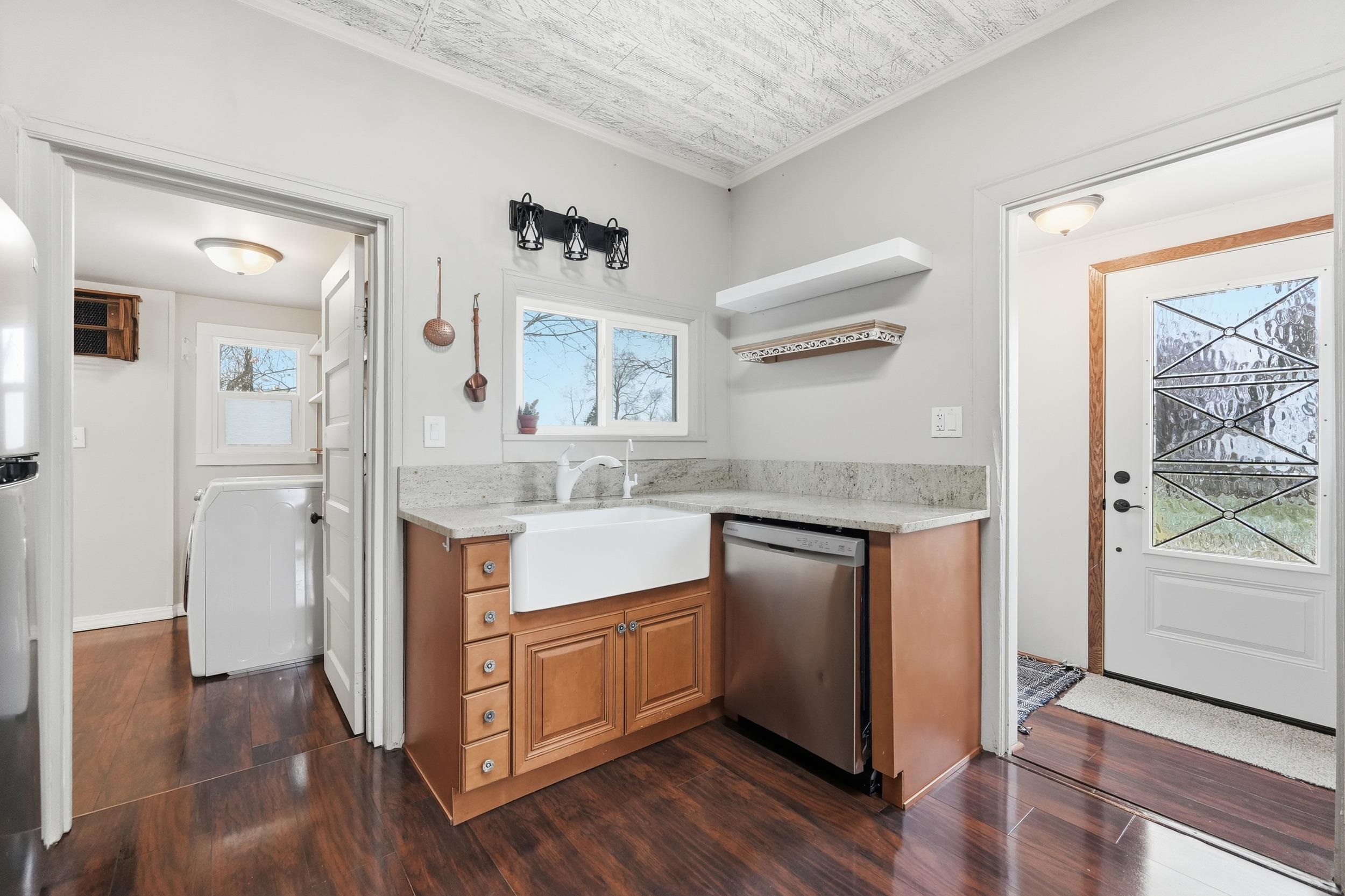 Kitchen with light stone countertops, brown cabinetry, stainless steel dishwasher, open shelves, and ornamental molding