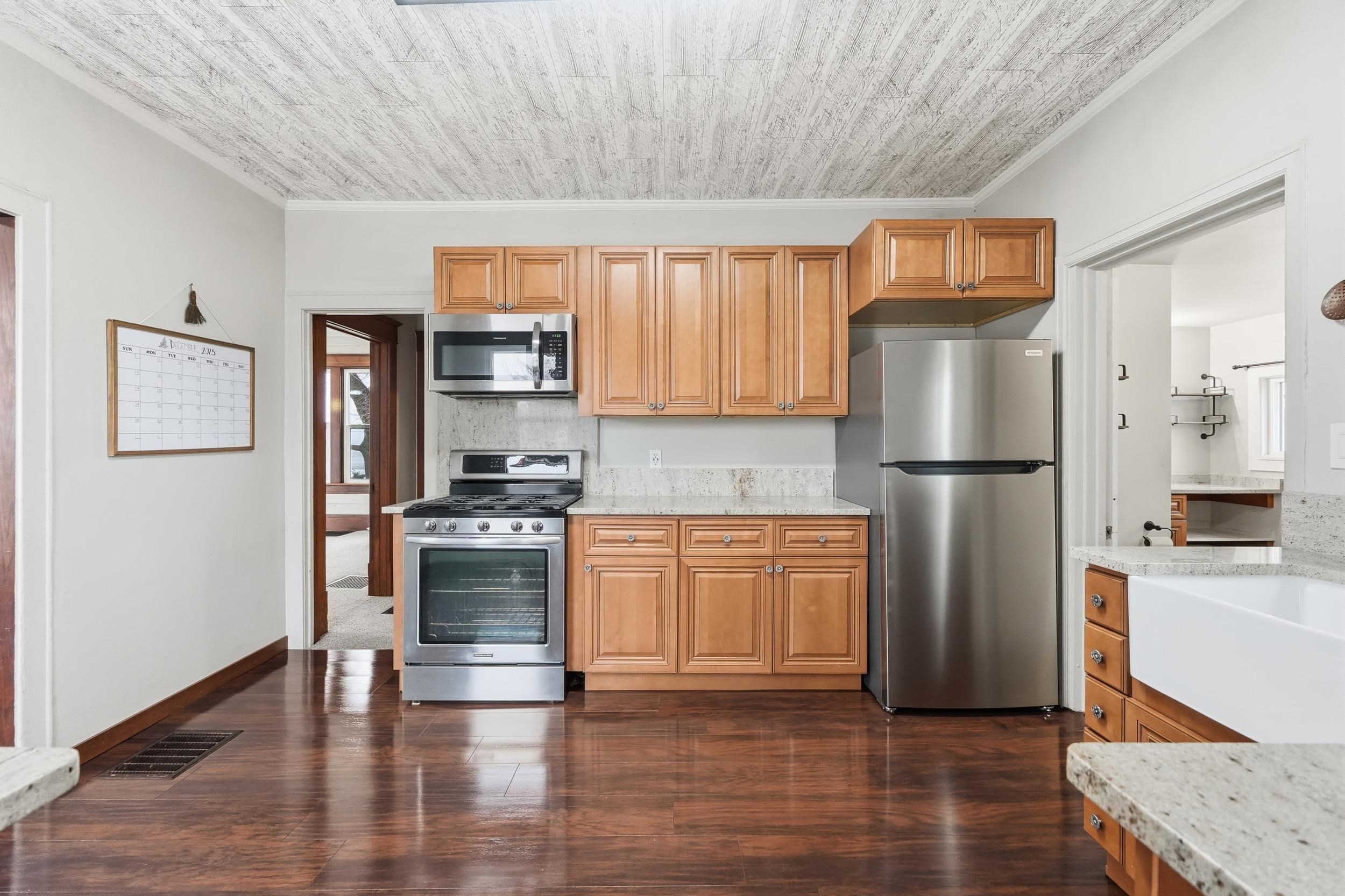 Kitchen featuring appliances with stainless steel finishes, crown molding, dark wood finished floors, light stone counters, and brown cabinetry