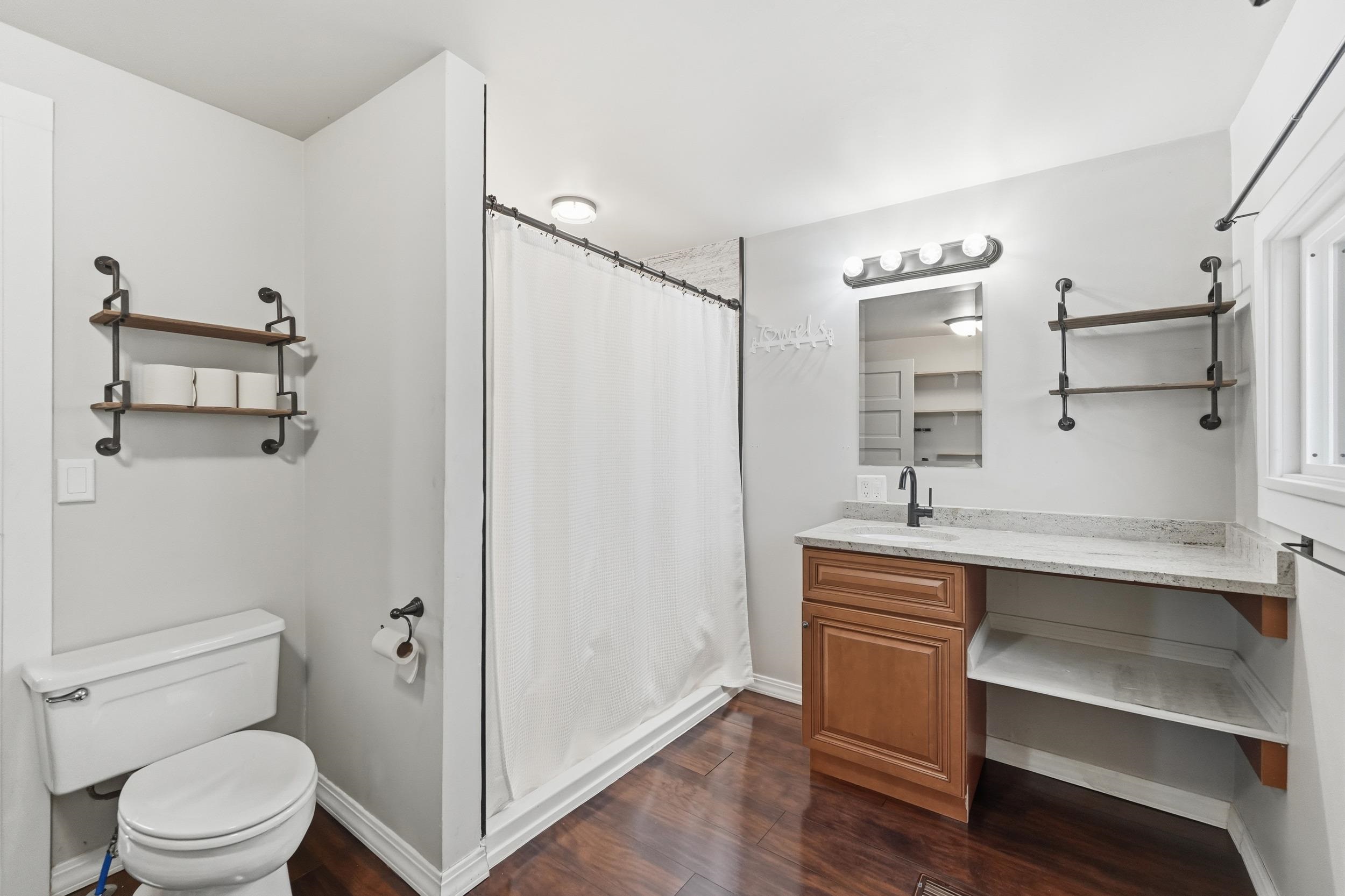 Full bath featuring curtained shower, vanity, and dark wood-type flooring