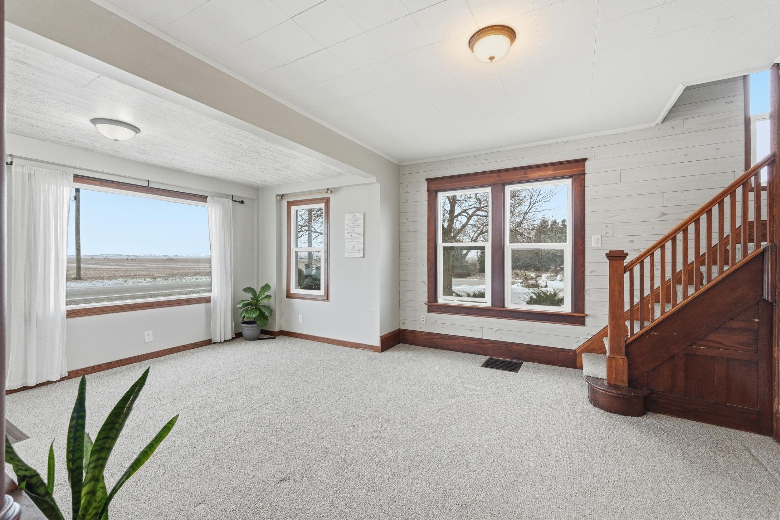 Unfurnished living room featuring carpet flooring, wooden walls, and stairway