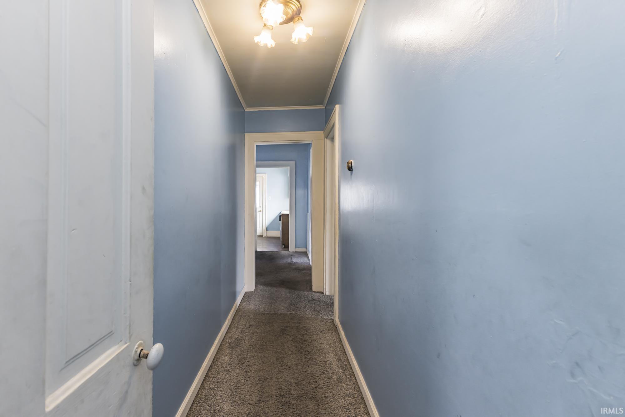 Hallway with dark colored carpet and ornamental molding