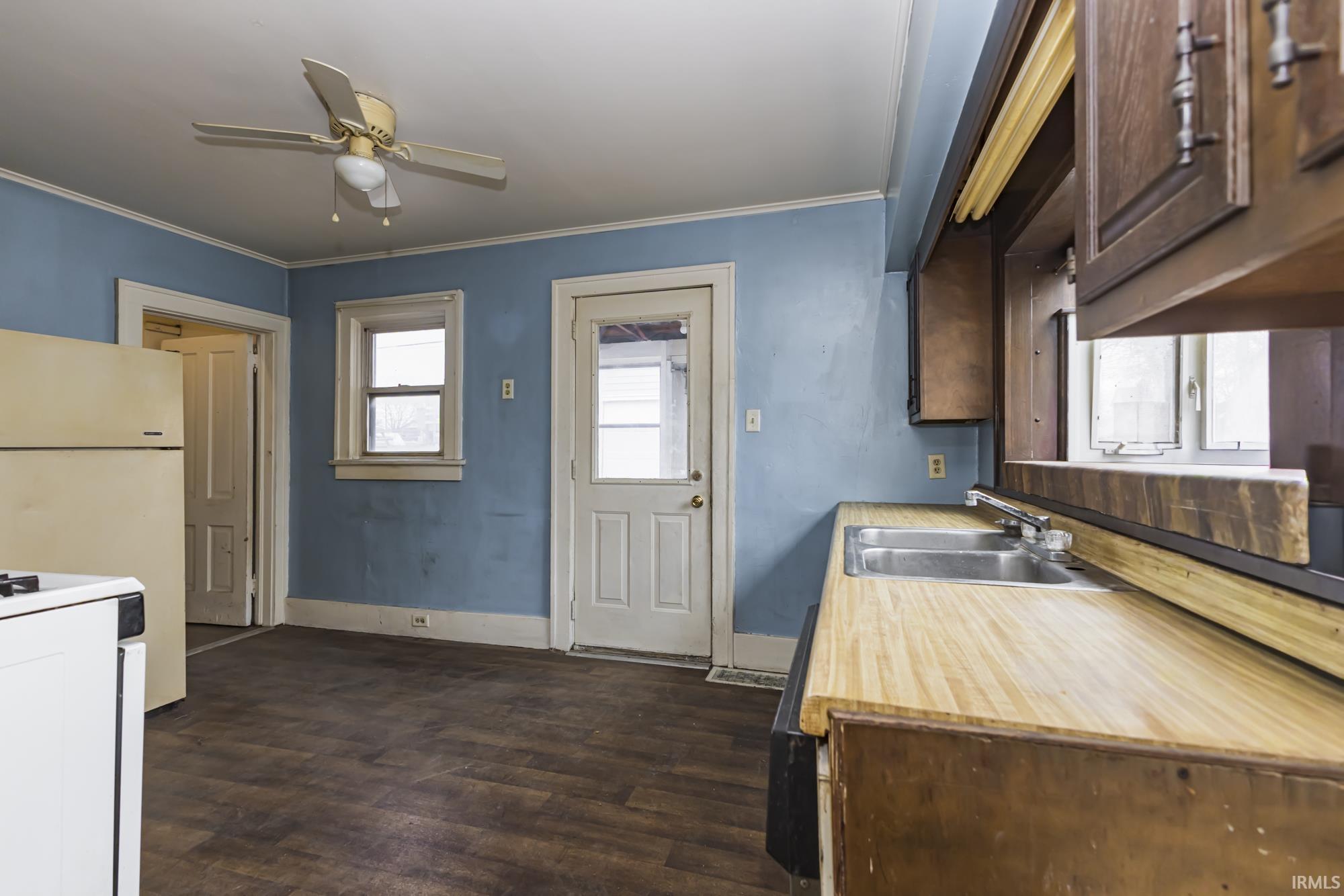 Kitchen featuring light countertops, white appliances, crown molding, dark wood-style flooring, and a ceiling fan
