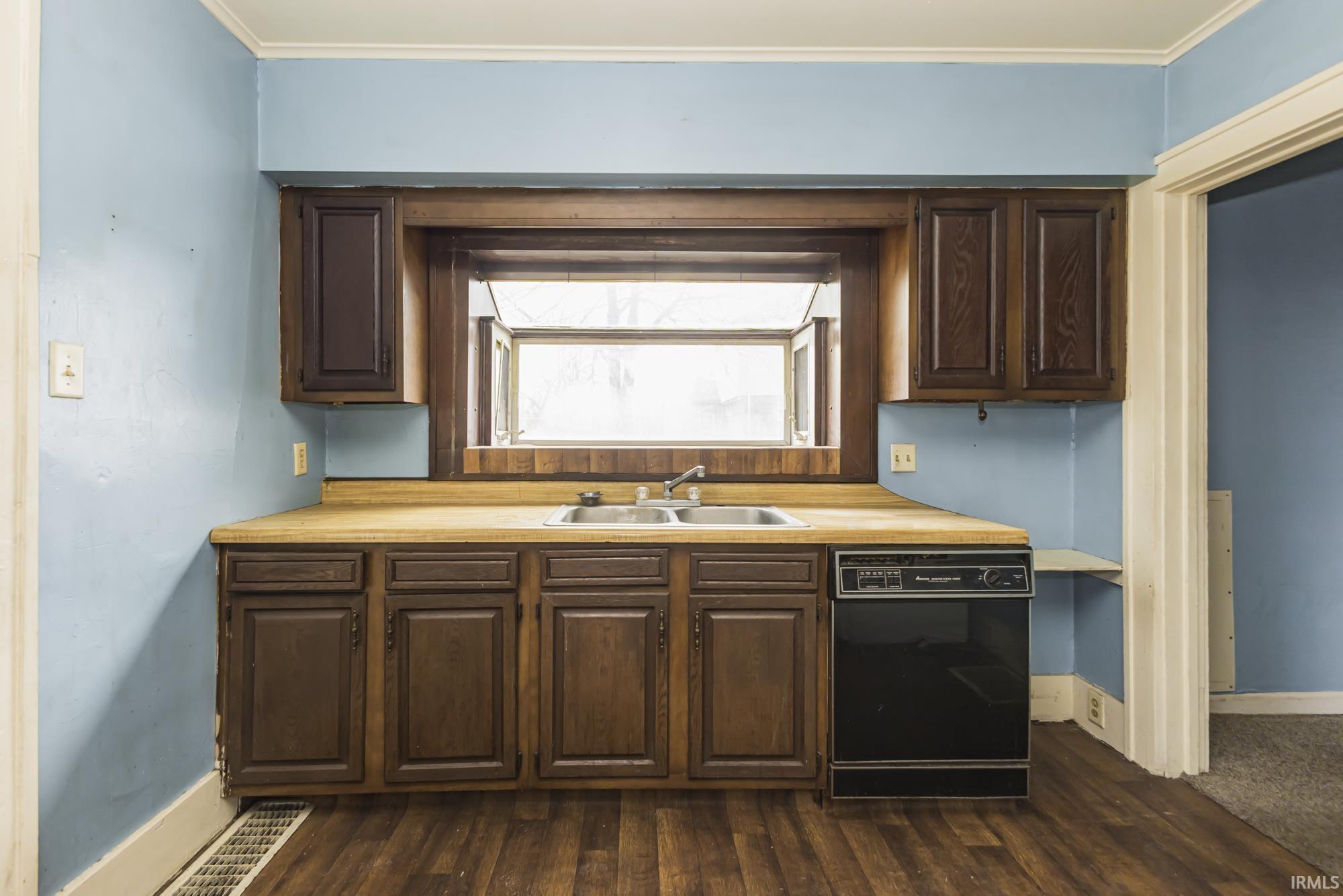 Kitchen featuring dark brown cabinetry, black dishwasher, light countertops, ornamental molding, and dark wood-type flooring