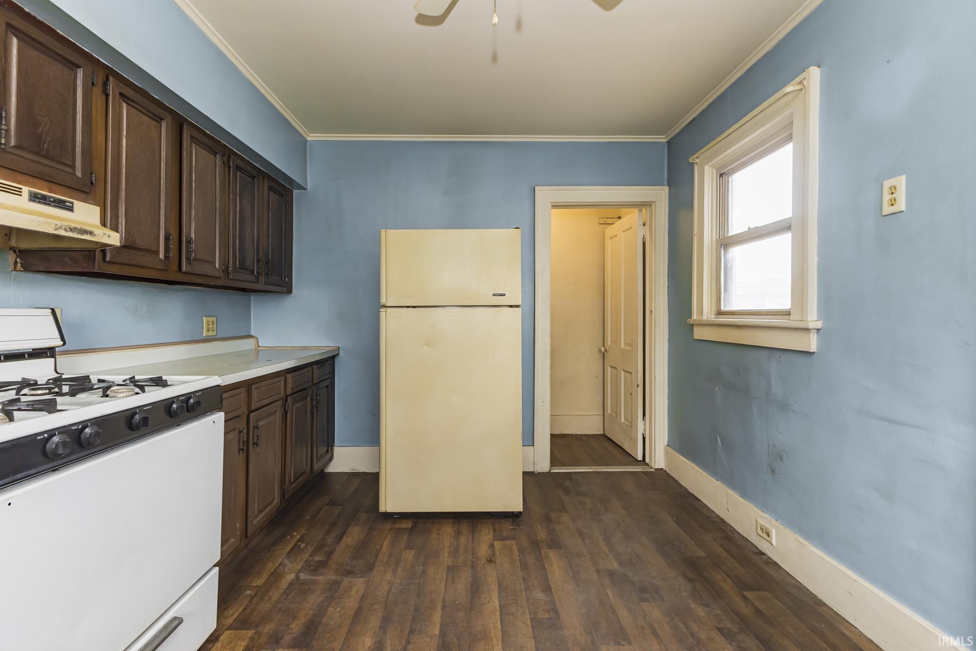 Kitchen with white appliances, dark brown cabinets, light countertops, dark wood-style floors, and ornamental molding