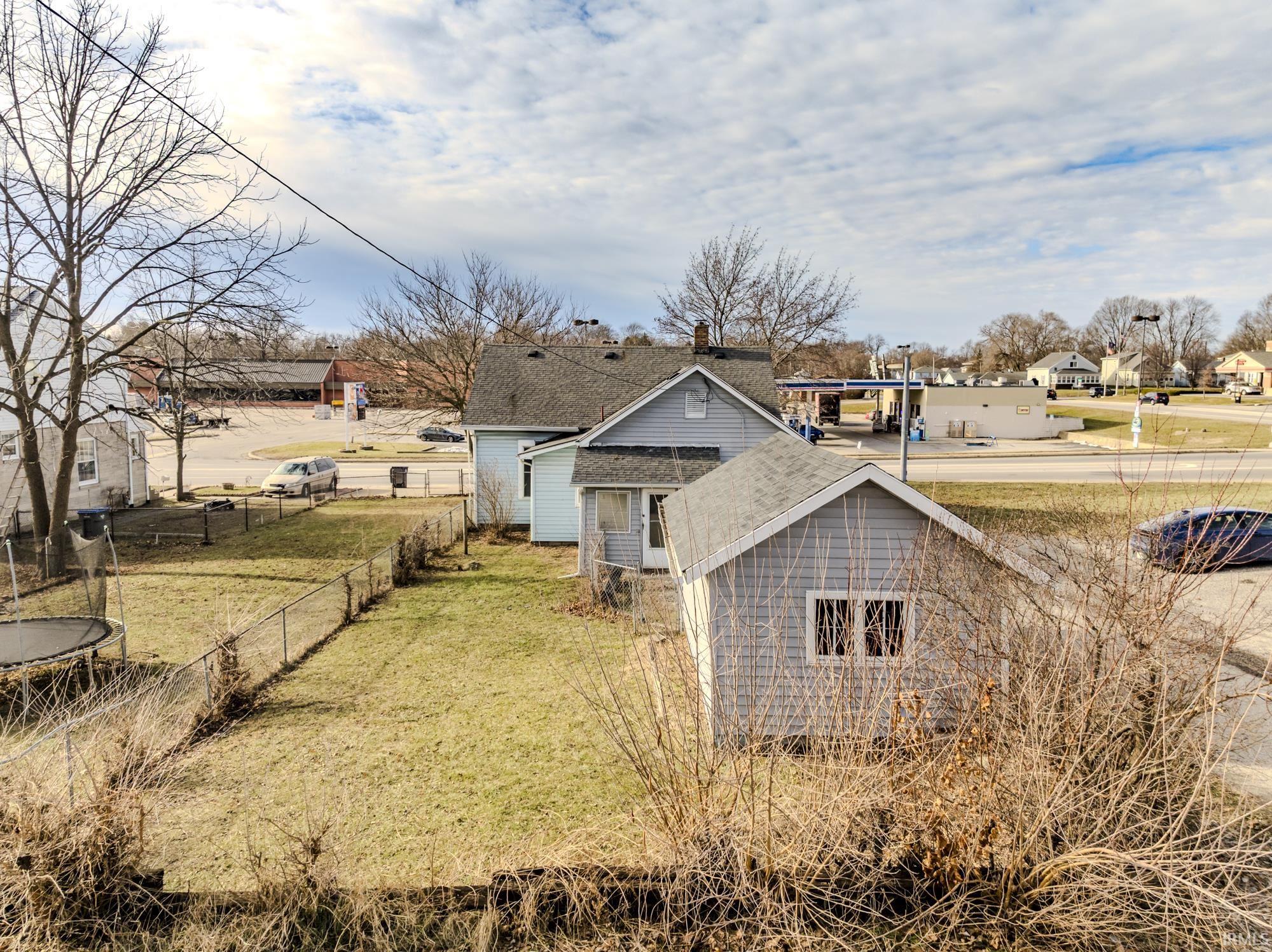 Back of house with a trampoline, a shingled roof, and a residential view