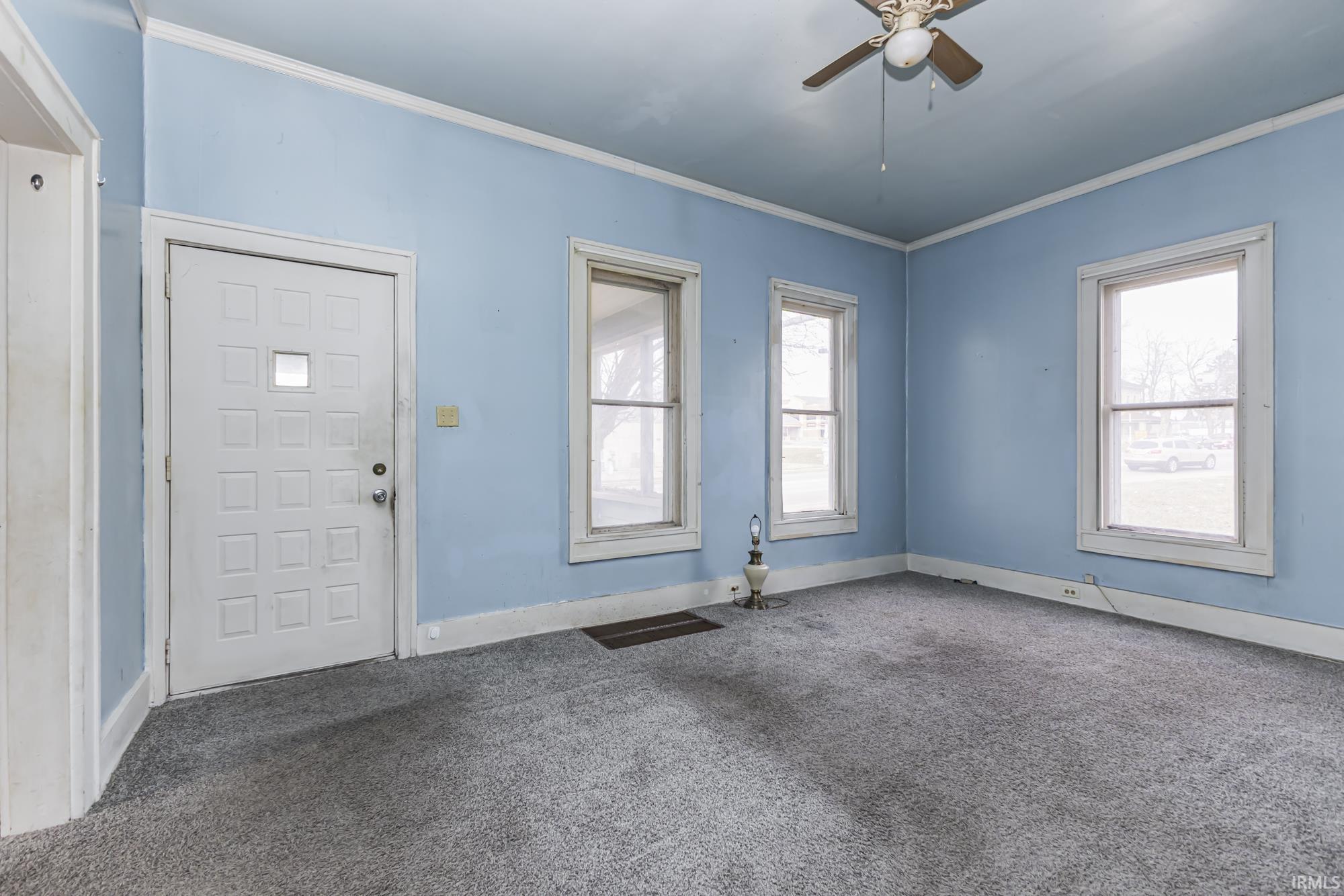 Foyer entrance with crown molding, carpet, and ceiling fan