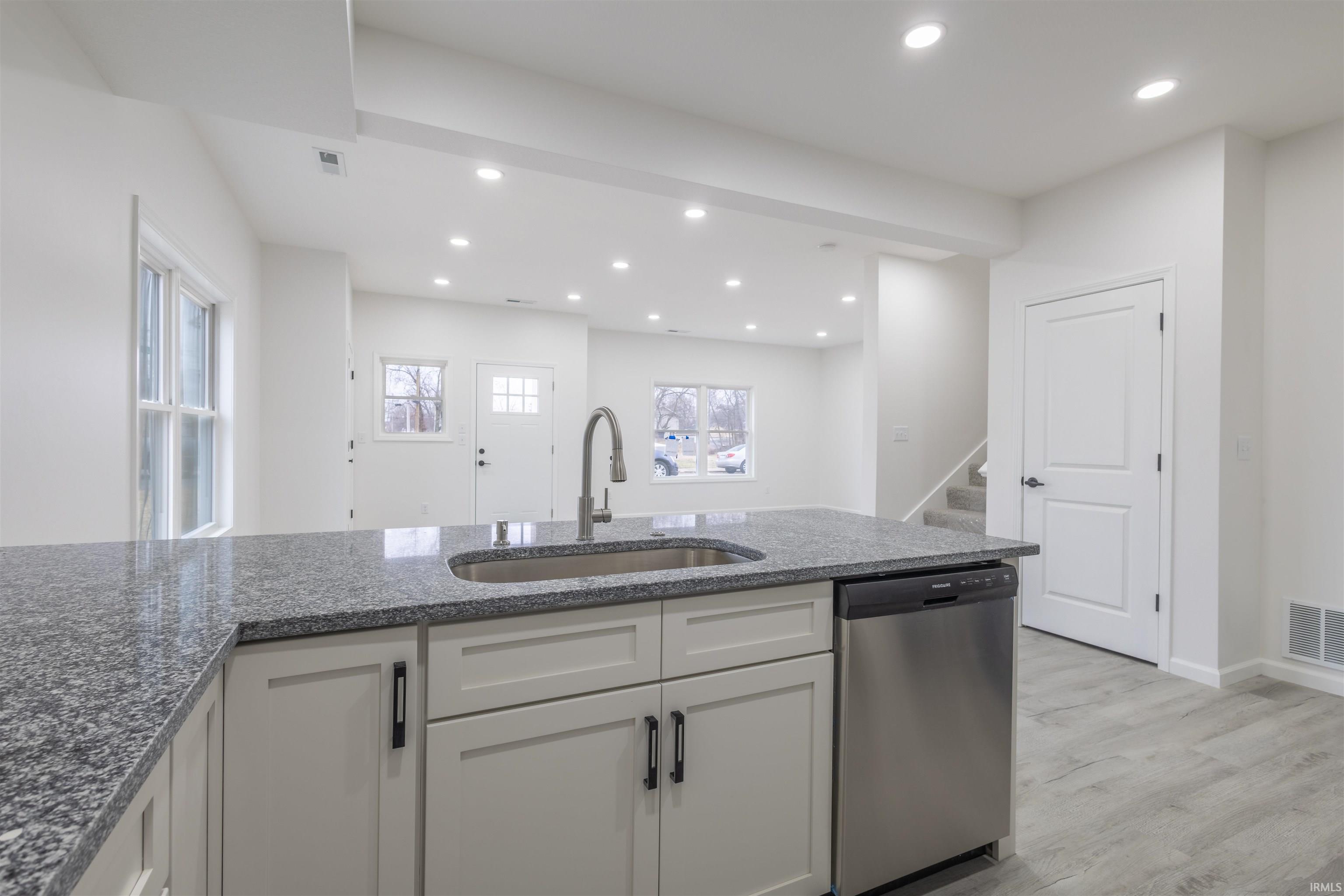 Kitchen featuring stainless steel dishwasher, dark stone counters, light wood-style flooring, white cabinets, and recessed lighting