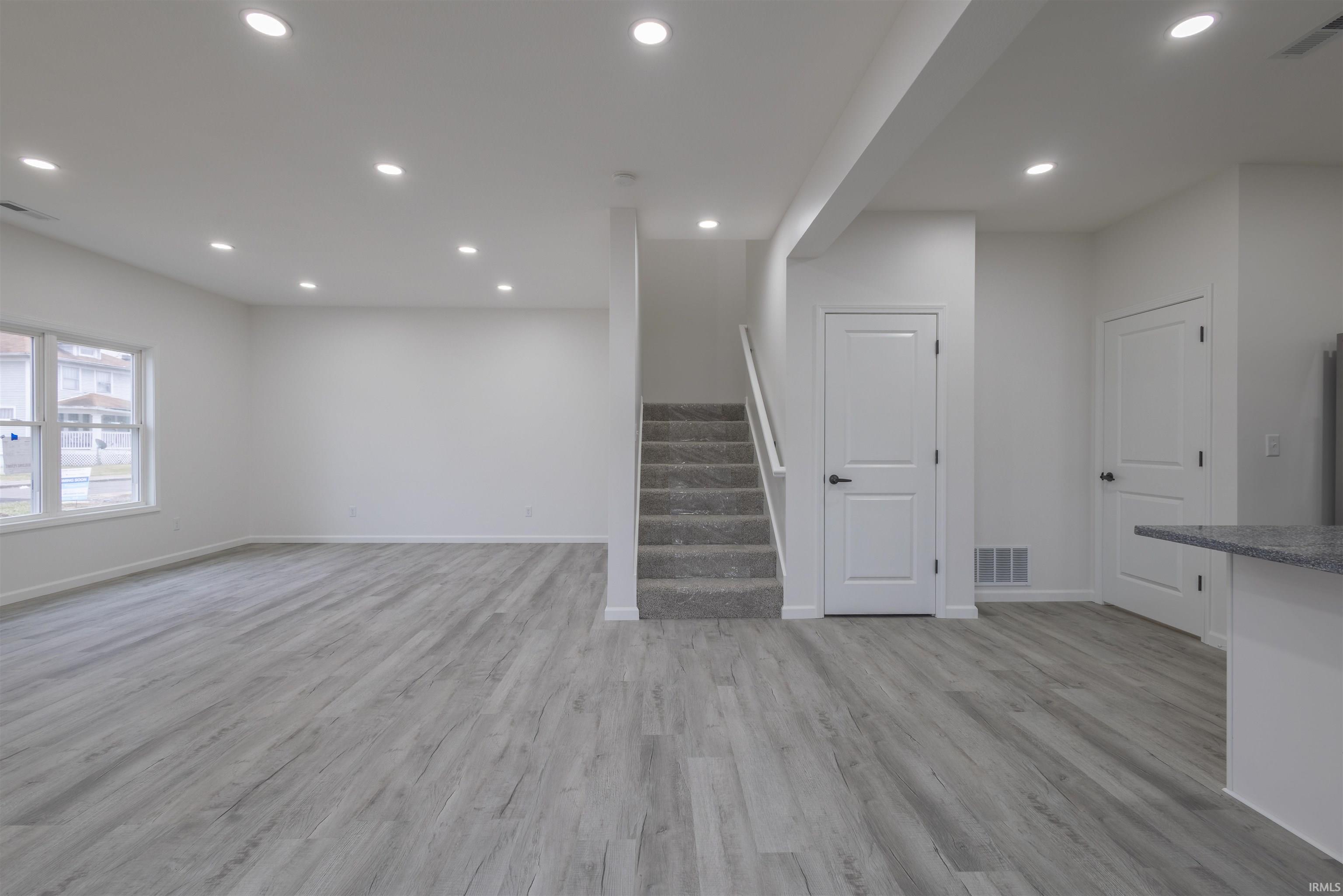Unfurnished living room featuring recessed lighting, light wood-style flooring, and stairway
