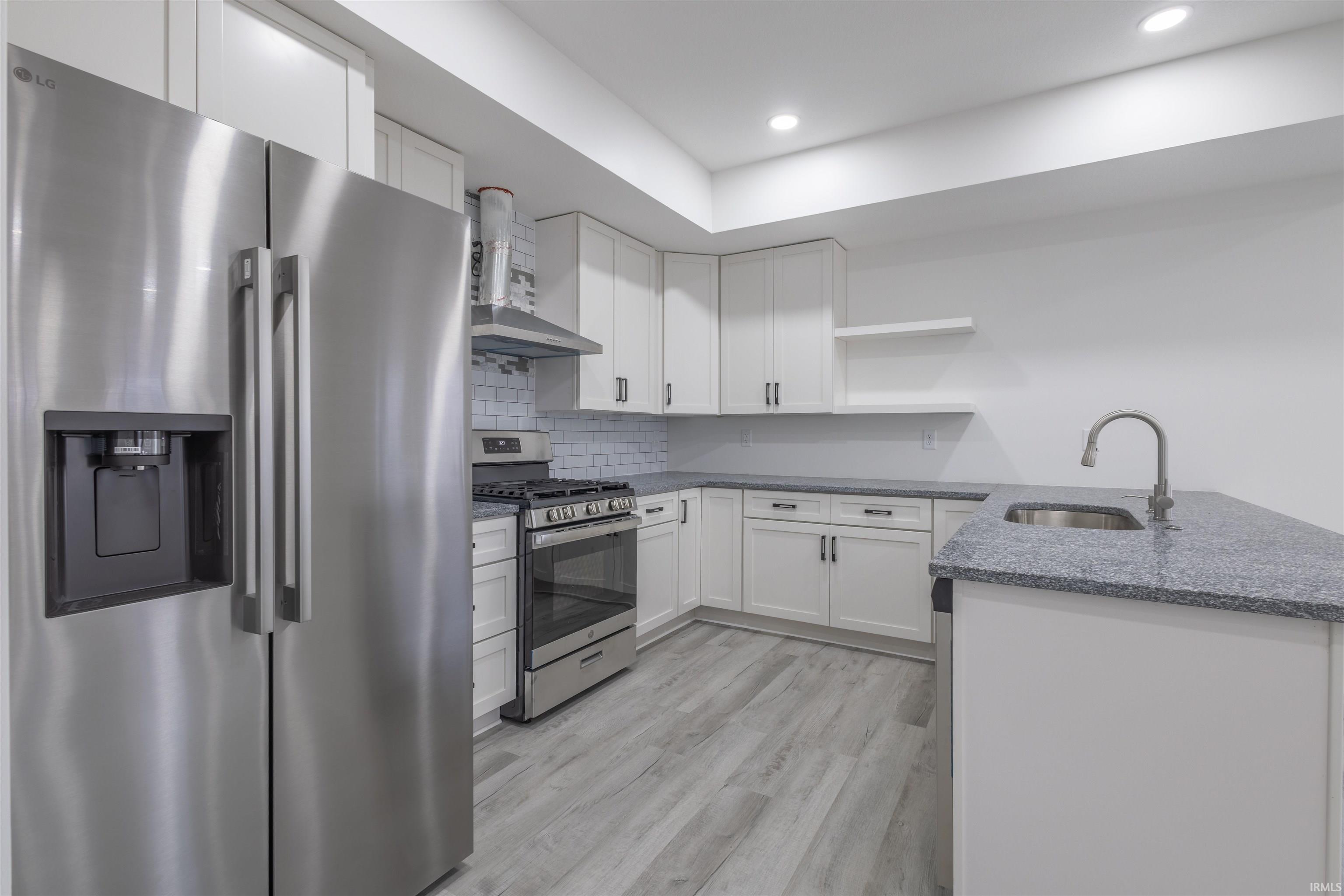 Kitchen featuring stainless steel appliances, open shelves, dark stone countertops, white cabinets, and wall chimney exhaust hood
