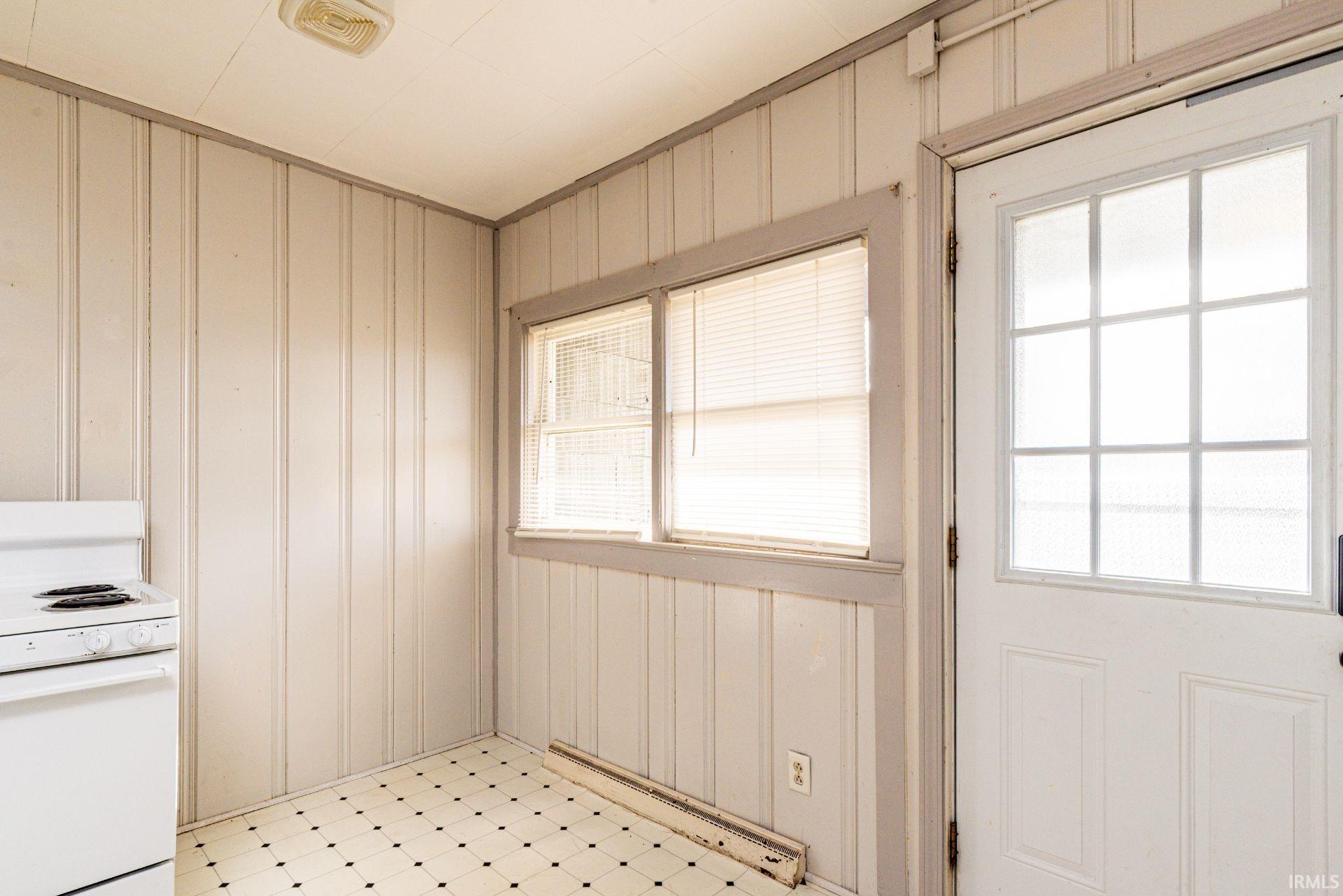 Kitchen with white electric range, a baseboard radiator, light floors, and wood walls
