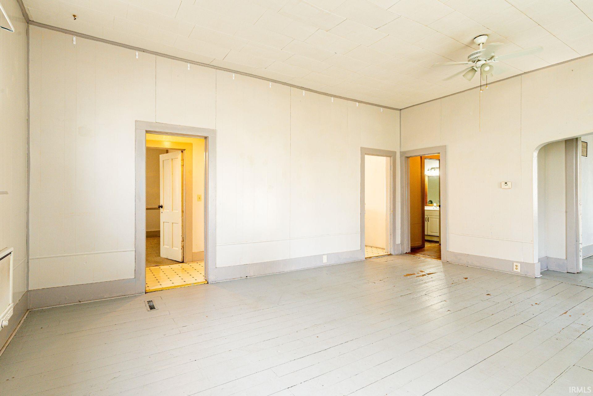 Spare room with arched walkways, ceiling fan, a towering ceiling, and light wood-style flooring