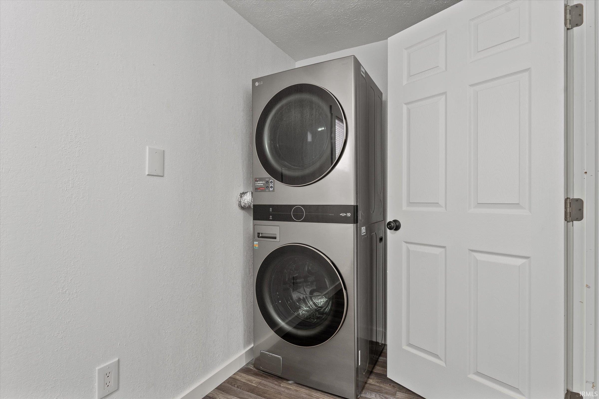 Washroom with dark wood-style flooring, stacked washer and clothes dryer, and a textured ceiling