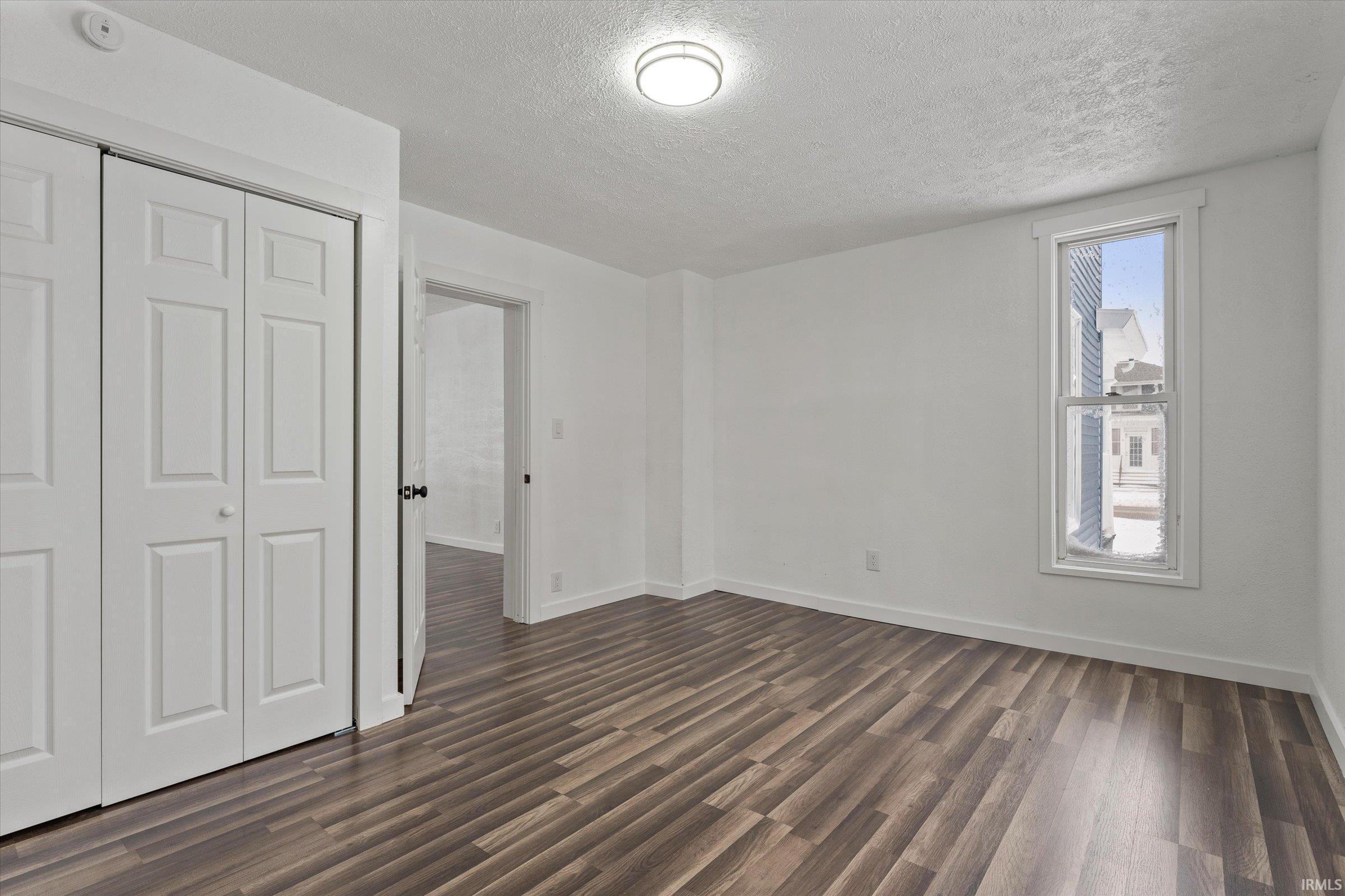Unfurnished bedroom featuring a textured ceiling, a closet, and dark wood-type flooring