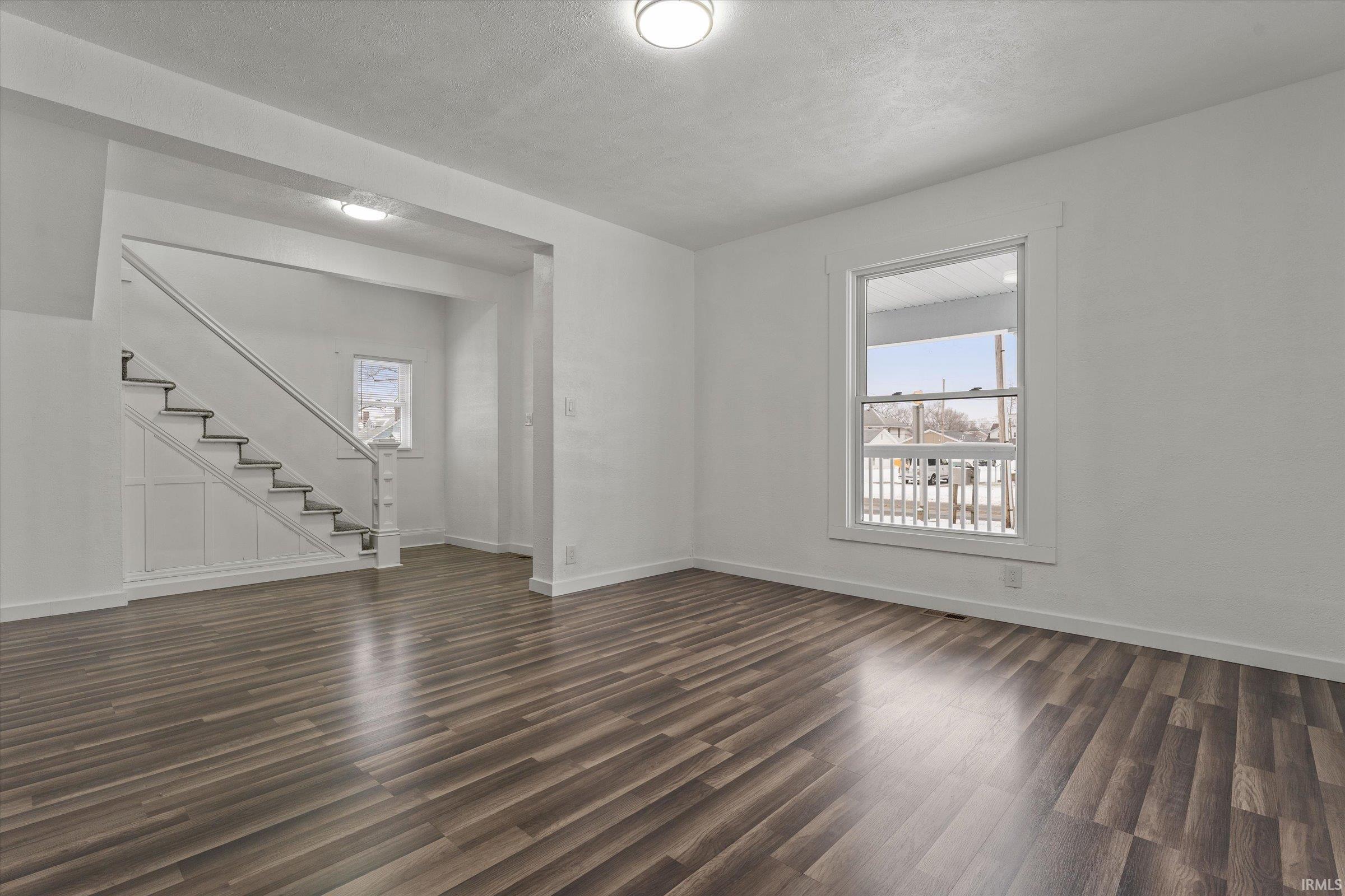Unfurnished living room with dark wood-type flooring and stairs