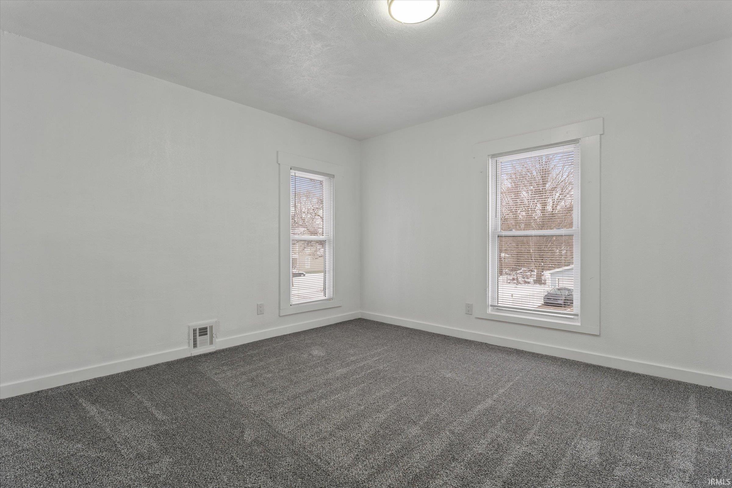 Empty room featuring dark carpet and a textured ceiling