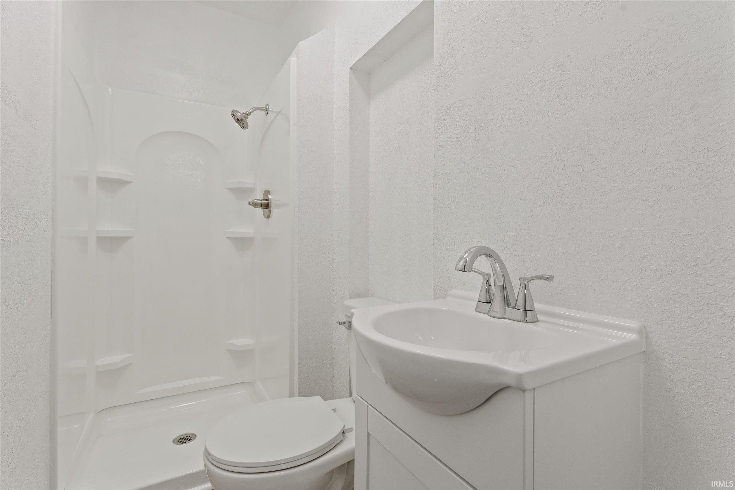 Bathroom featuring a textured wall, vanity, and a shower stall