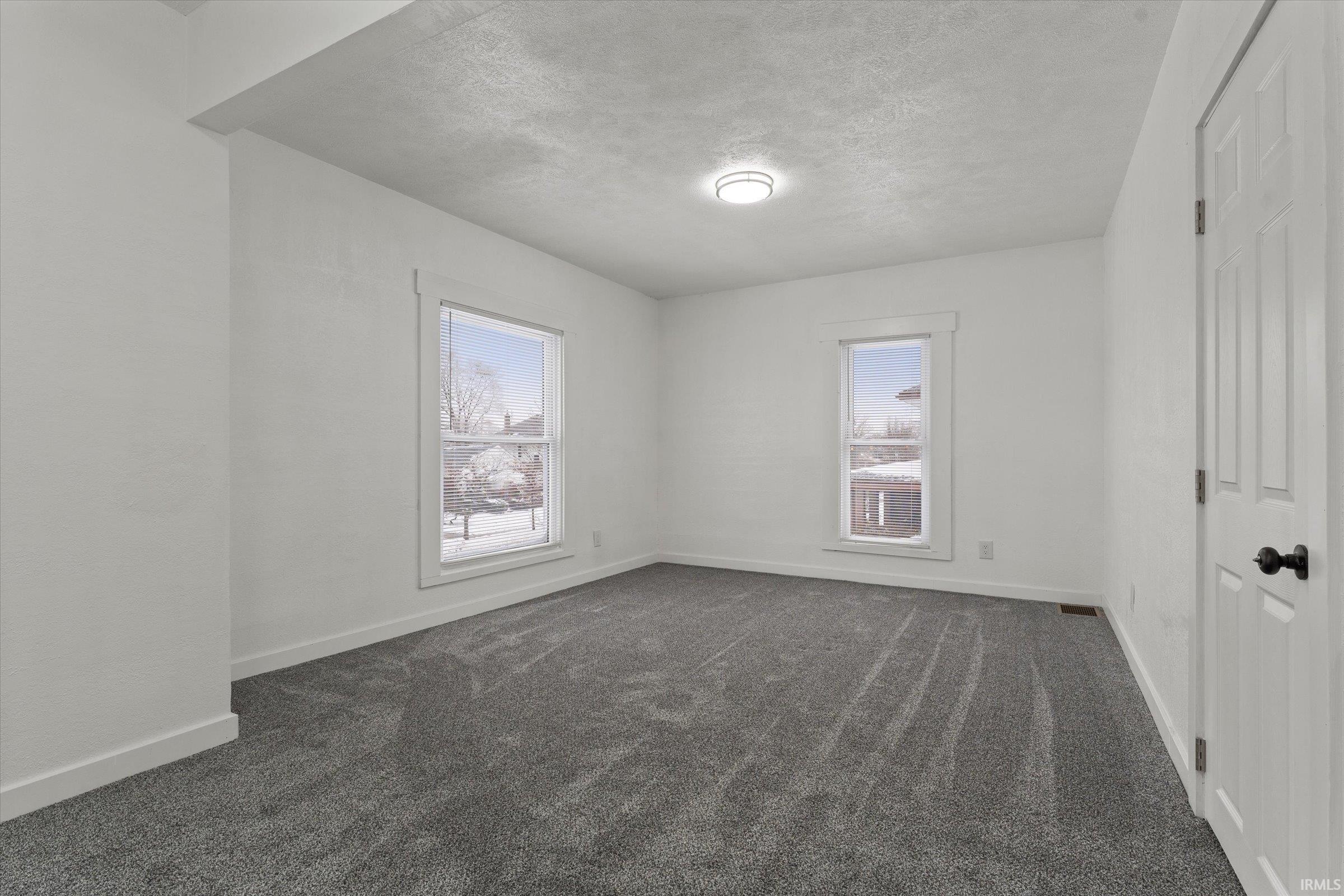 Spare room featuring plenty of natural light, a textured ceiling, and dark colored carpet