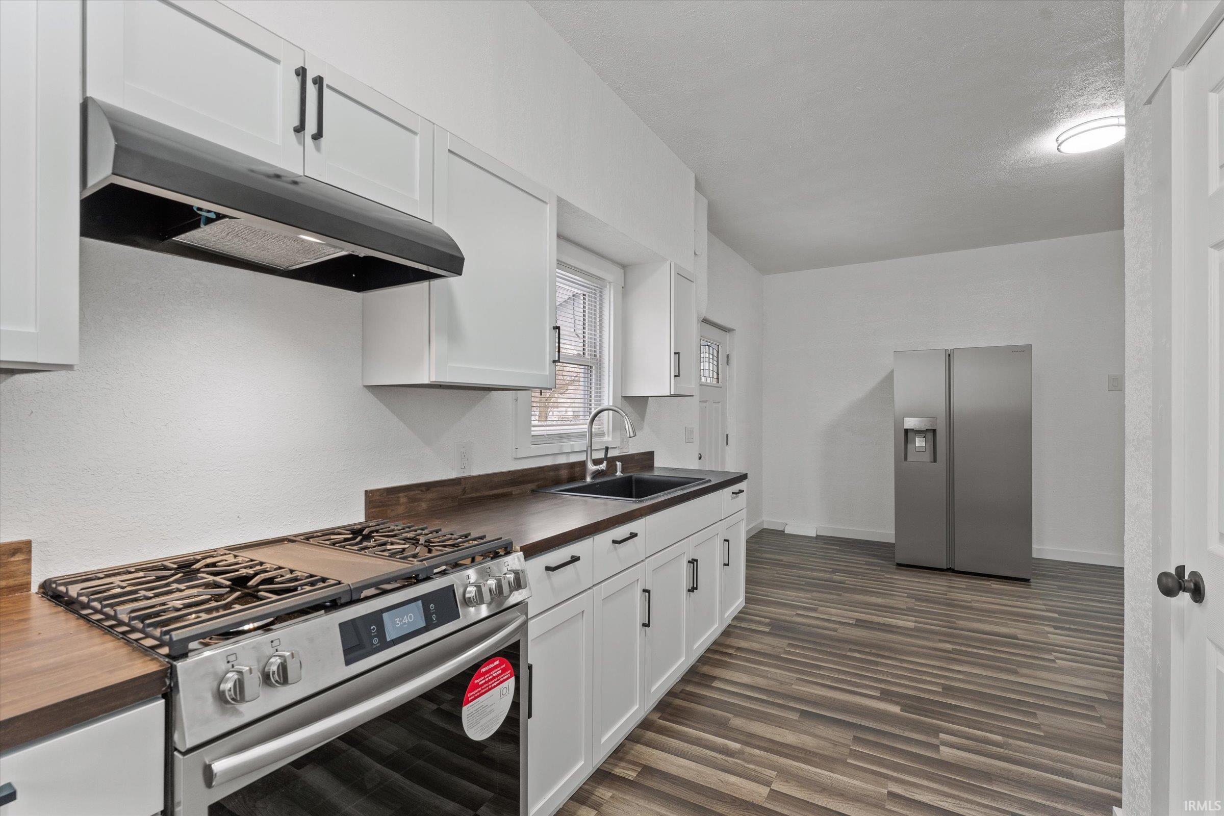 Kitchen featuring appliances with stainless steel finishes, white cabinetry, under cabinet range hood, dark wood finished floors, and wooden counters