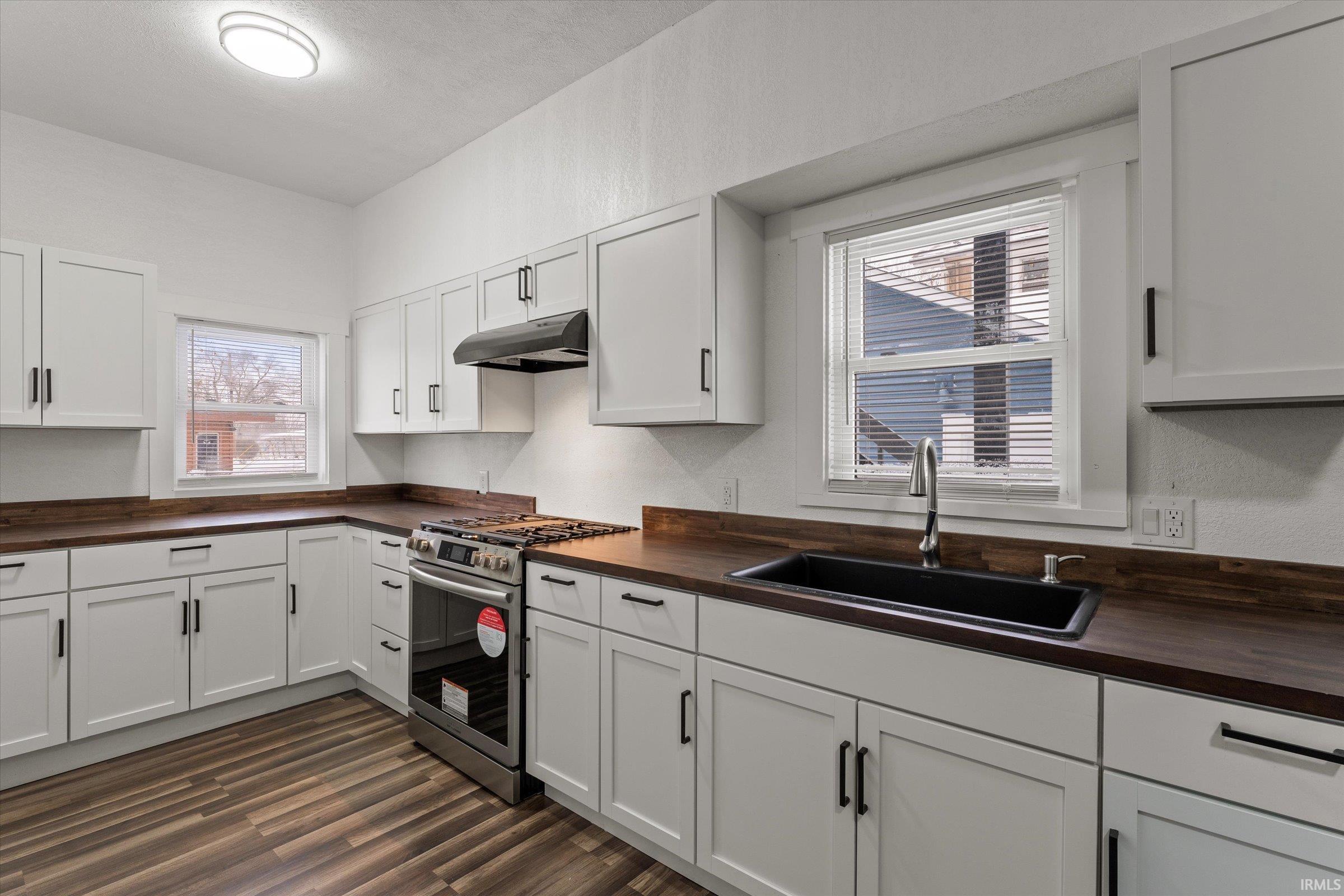 Kitchen featuring butcher block counters, stainless steel range with gas cooktop, white cabinets, dark wood finished floors, and under cabinet range hood