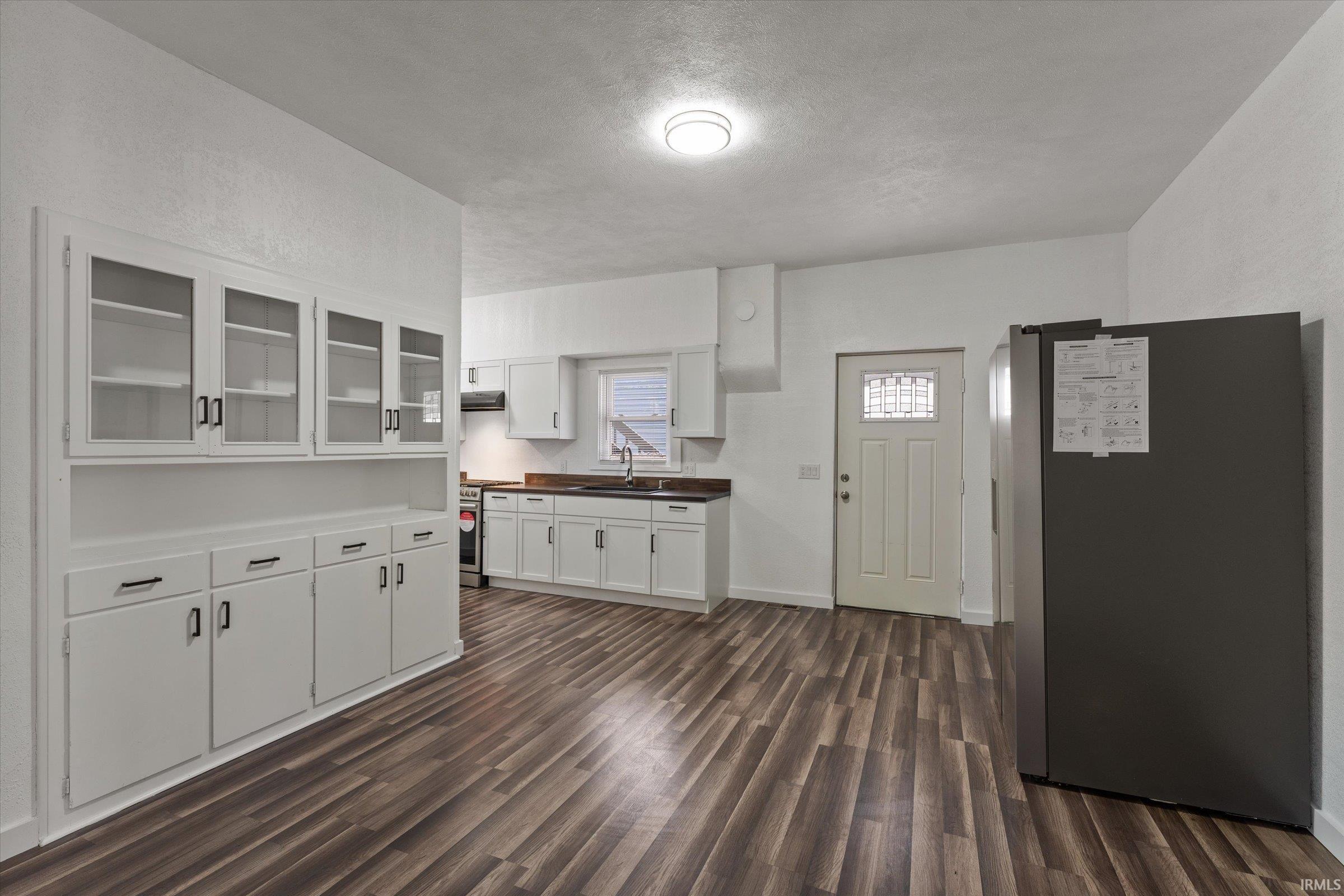Kitchen featuring white cabinetry, appliances with stainless steel finishes, glass insert cabinets, dark wood-type flooring, and a textured ceiling