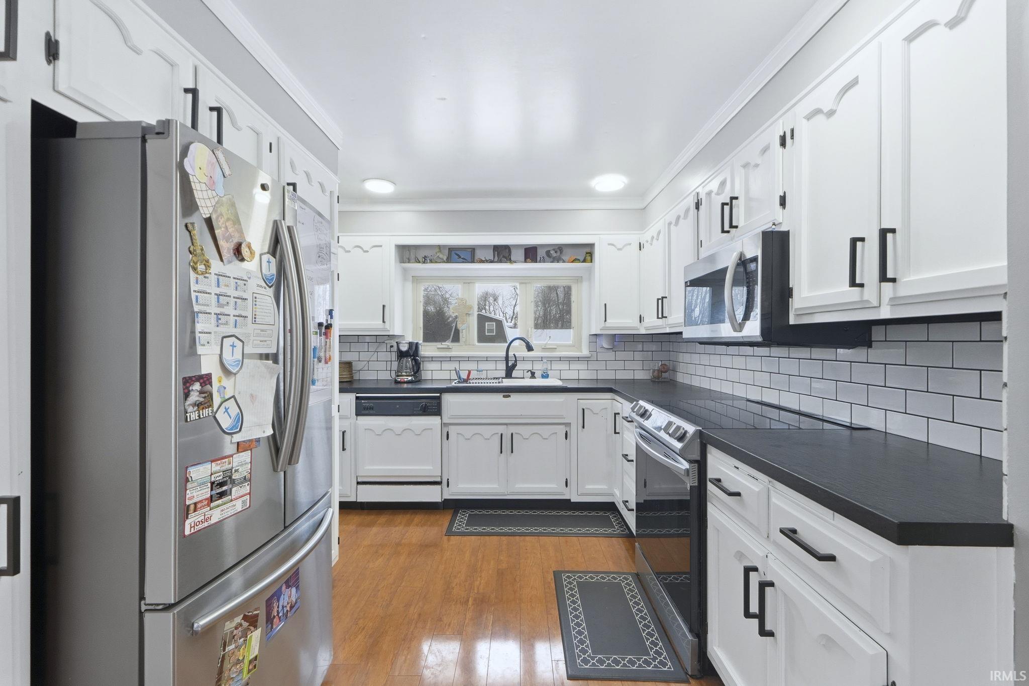 Kitchen featuring stainless steel appliances, dark countertops, white cabinets, dark wood-style floors, and decorative backsplash