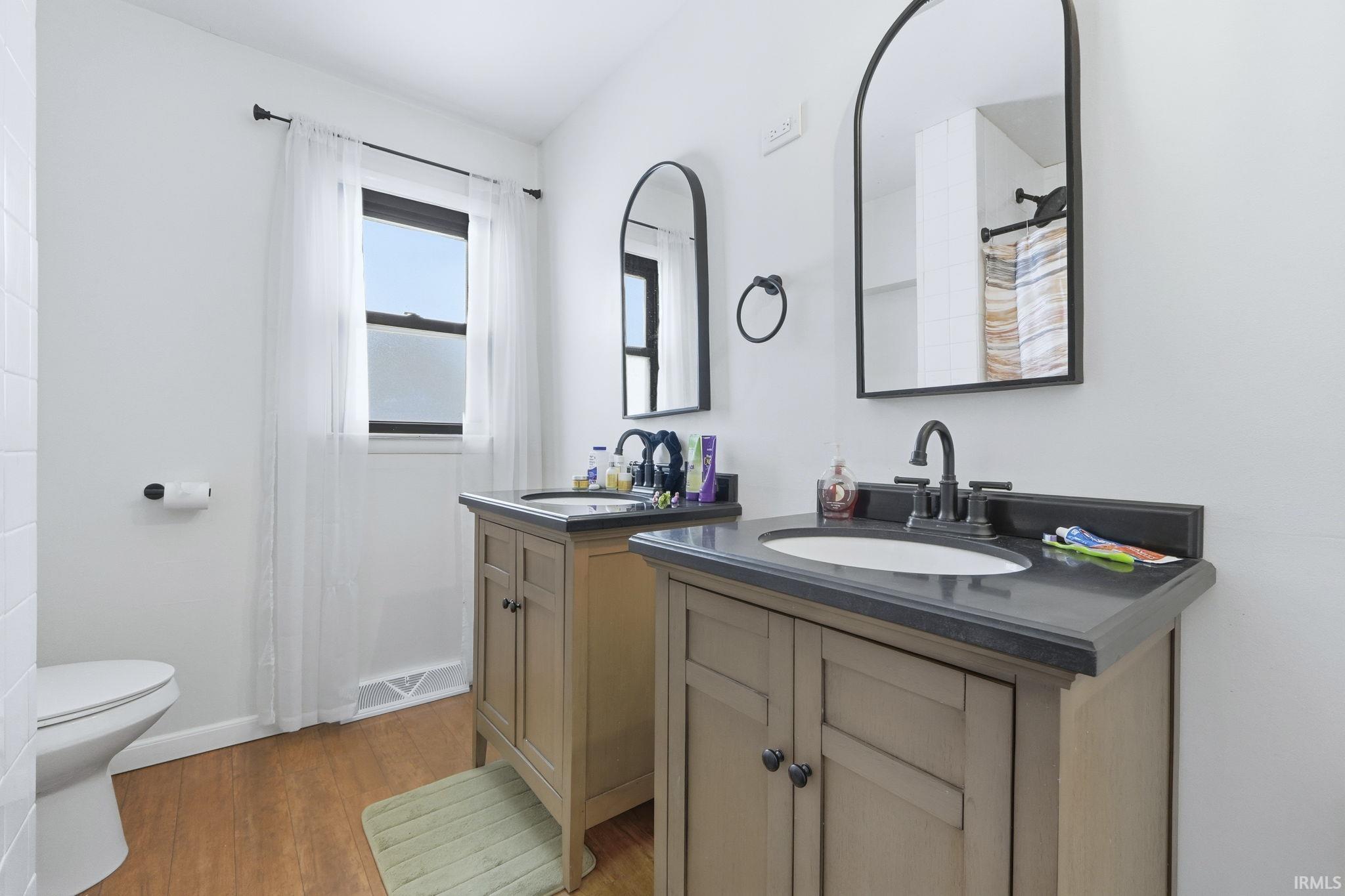 Bathroom with a shower with curtain, two vanities, and light wood-style floors