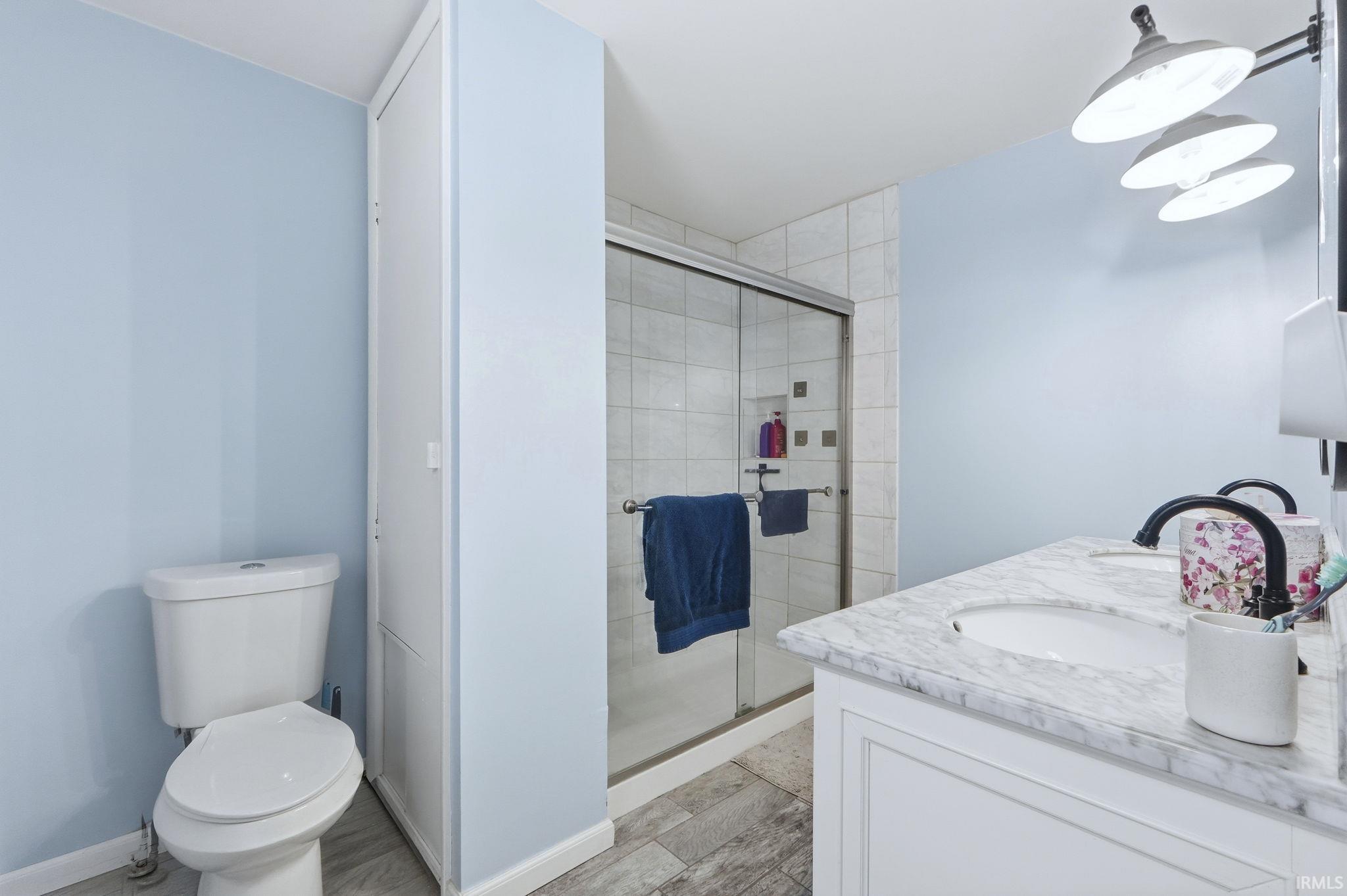 Bathroom with double vanity, a shower stall, and wood finish floors