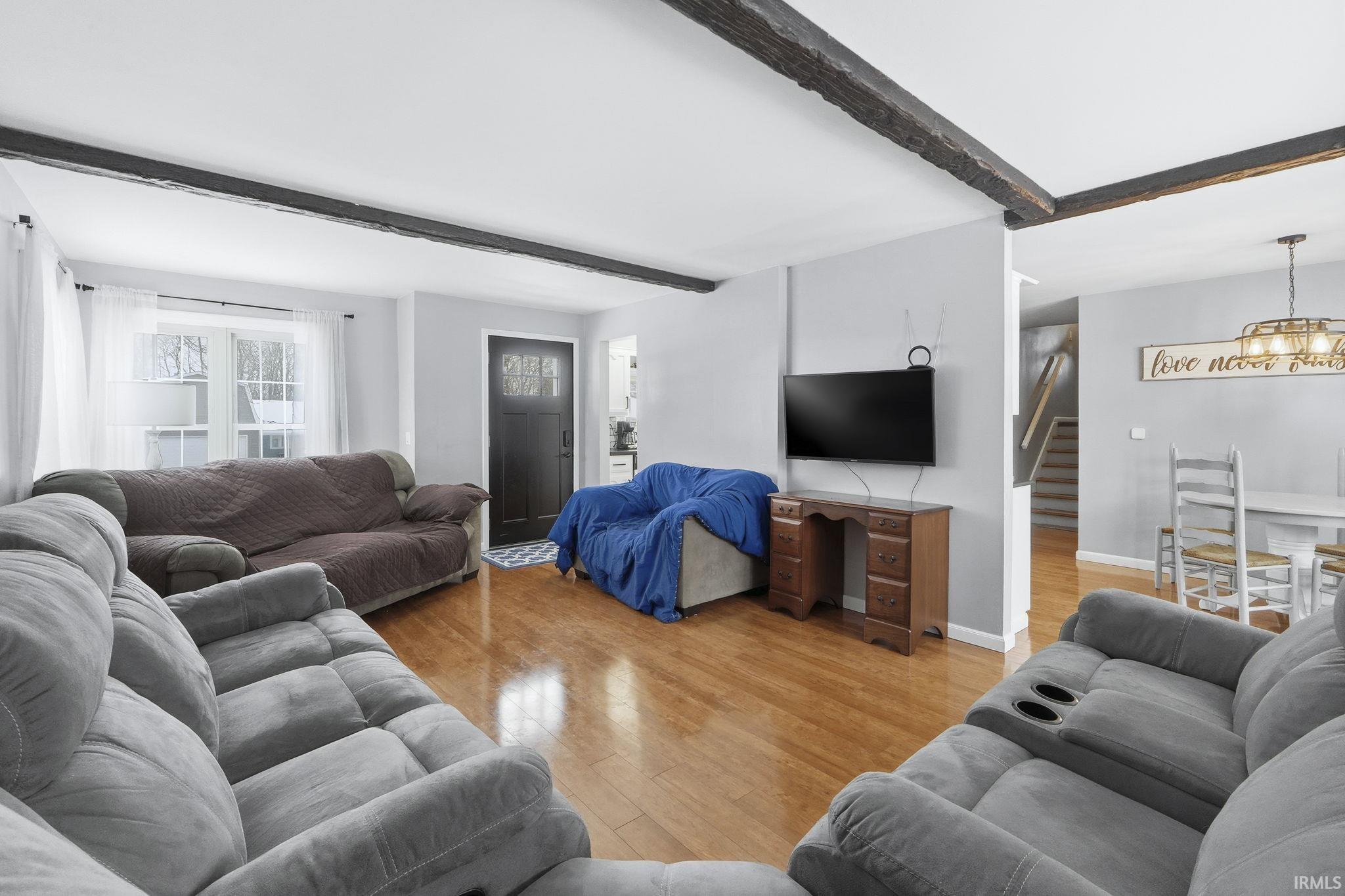 Living room with light wood finished floors, beam ceiling, a chandelier, and stairs
