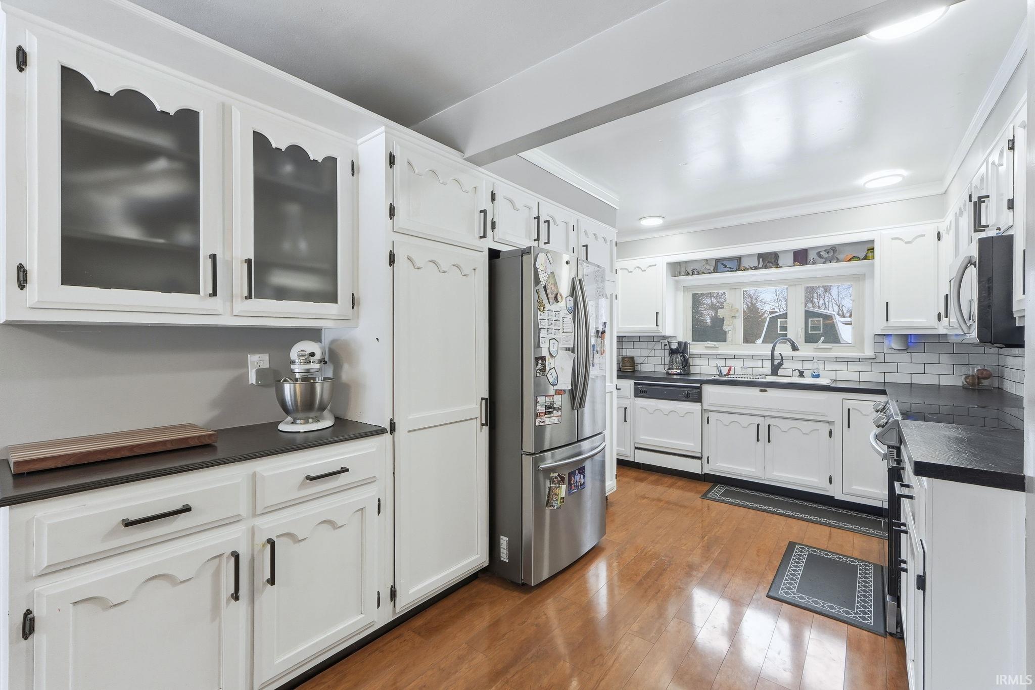 Kitchen featuring dark countertops, stainless steel appliances, white cabinetry, dark wood-style flooring, and glass insert cabinets