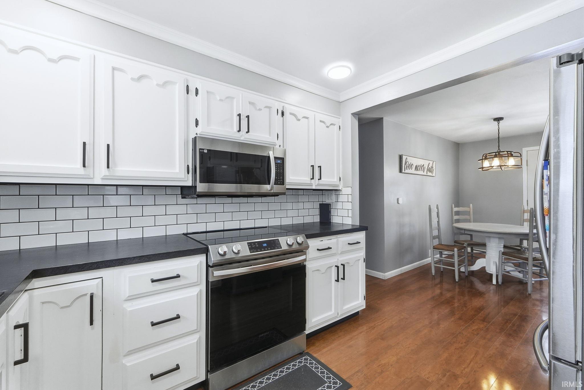 Kitchen with stainless steel appliances, white cabinets, tasteful backsplash, dark wood-style flooring, and decorative light fixtures