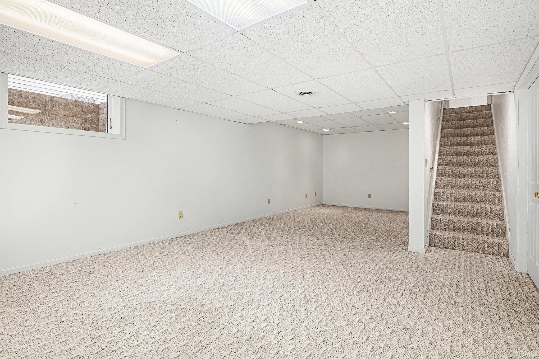 Finished below grade area featuring carpet flooring, a paneled ceiling, and stairs