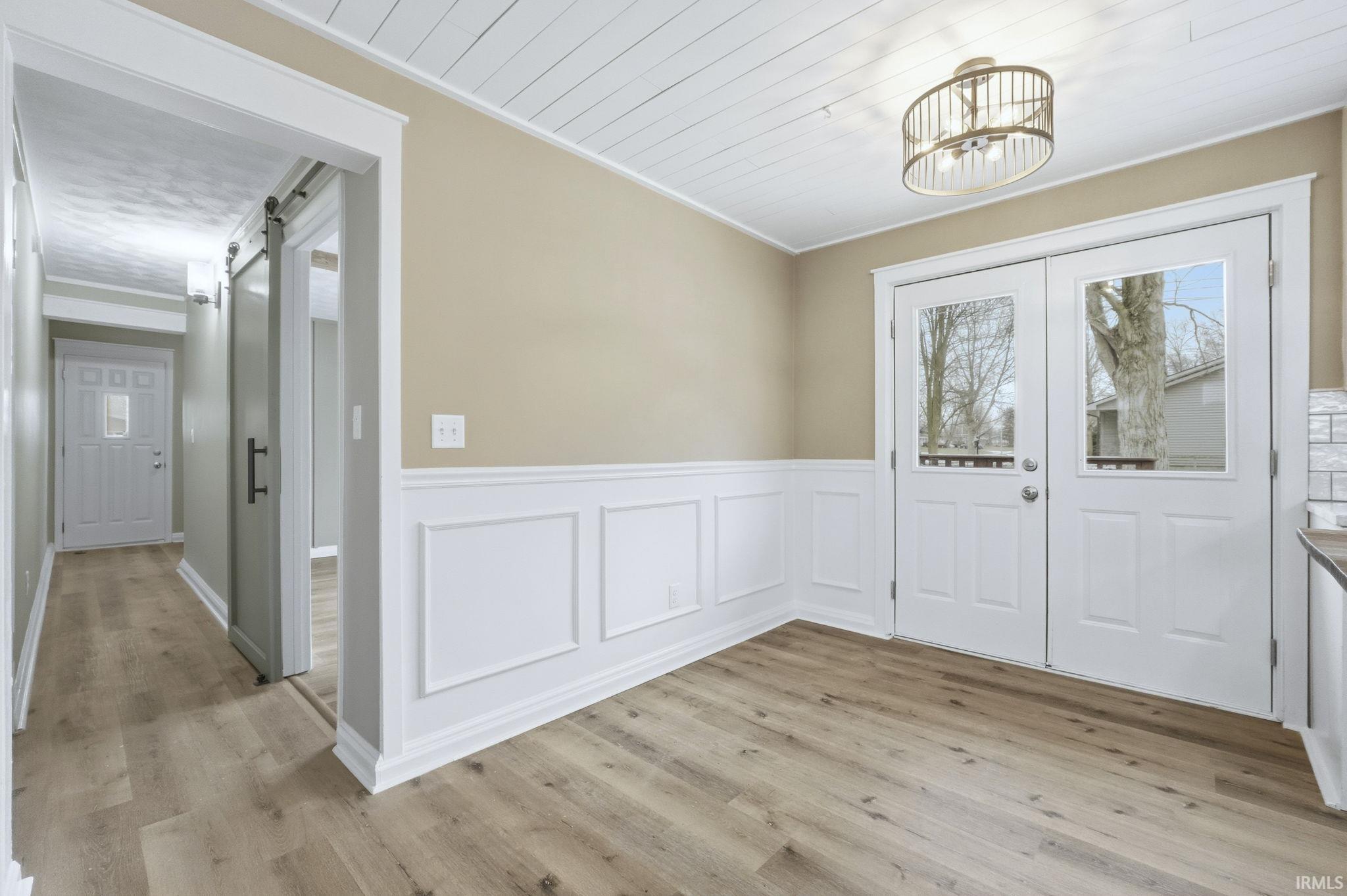Unfurnished dining area featuring a barn door, light wood-style flooring, a decorative wall, wainscoting, and a chandelier