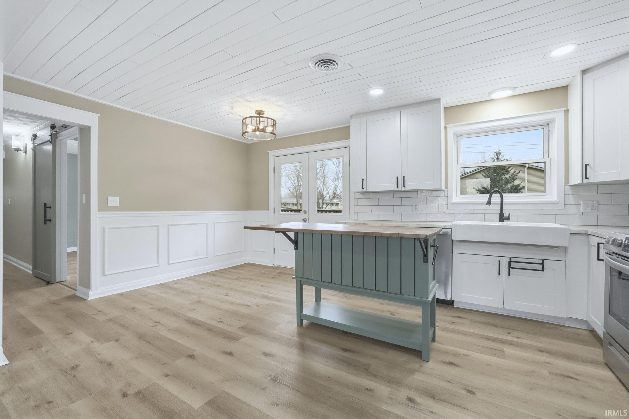Kitchen with wainscoting, white cabinets, a decorative wall, light wood finished floors, and wooden ceiling