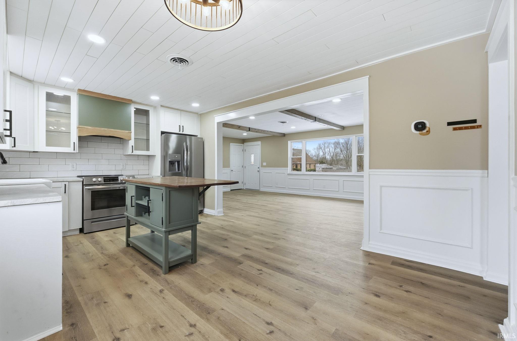 Kitchen featuring a decorative wall, white cabinets, glass insert cabinets, a wainscoted wall, and light wood-style floors