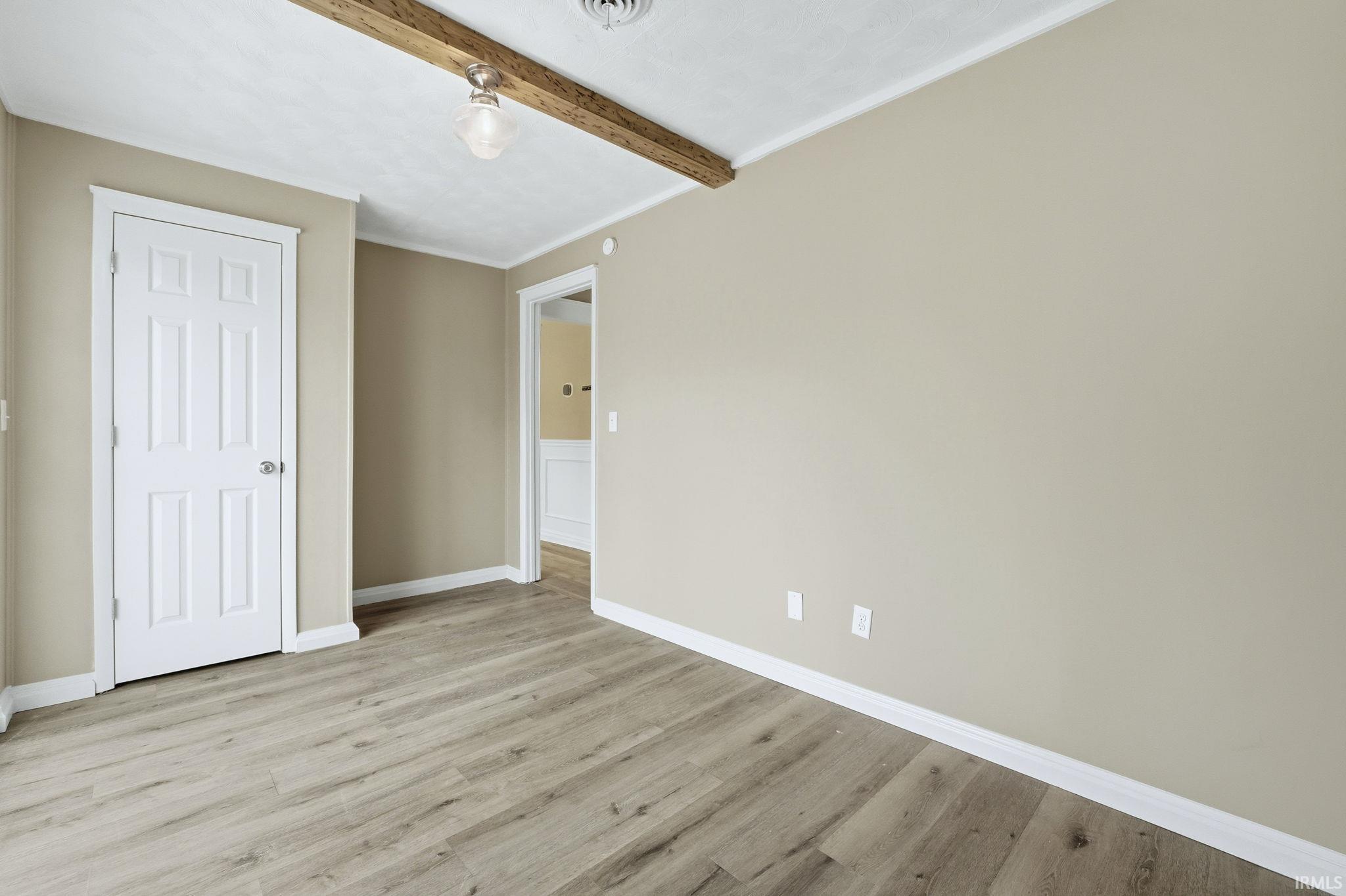 Unfurnished bedroom featuring light wood-style flooring, beamed ceiling, and crown molding