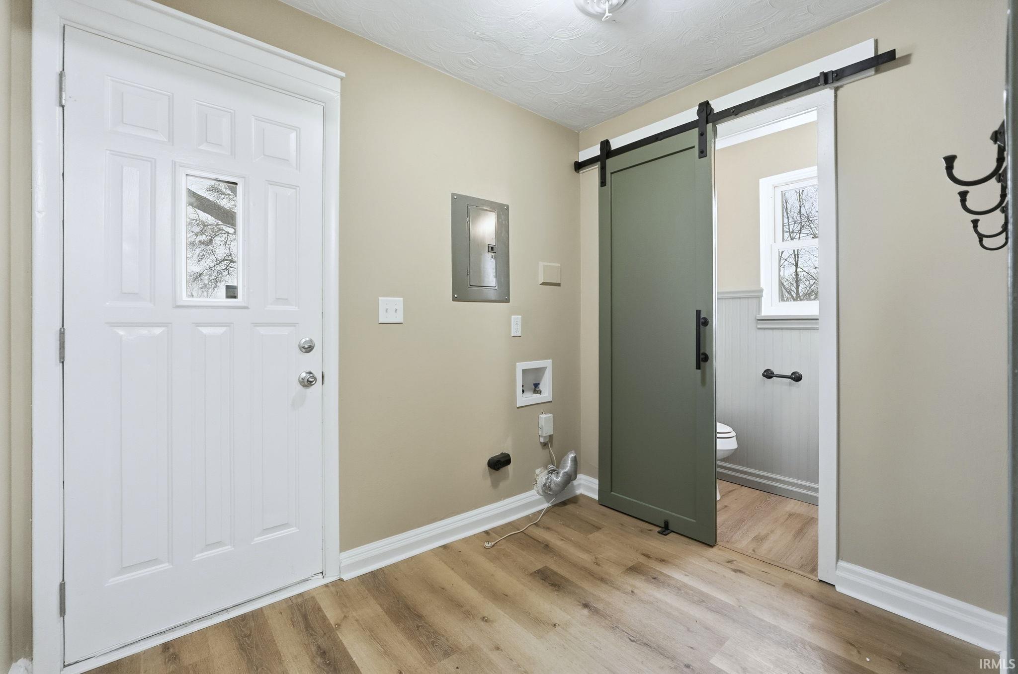 Laundry room with a barn door, electric panel, light wood finished floors, and hookup for a washing machine