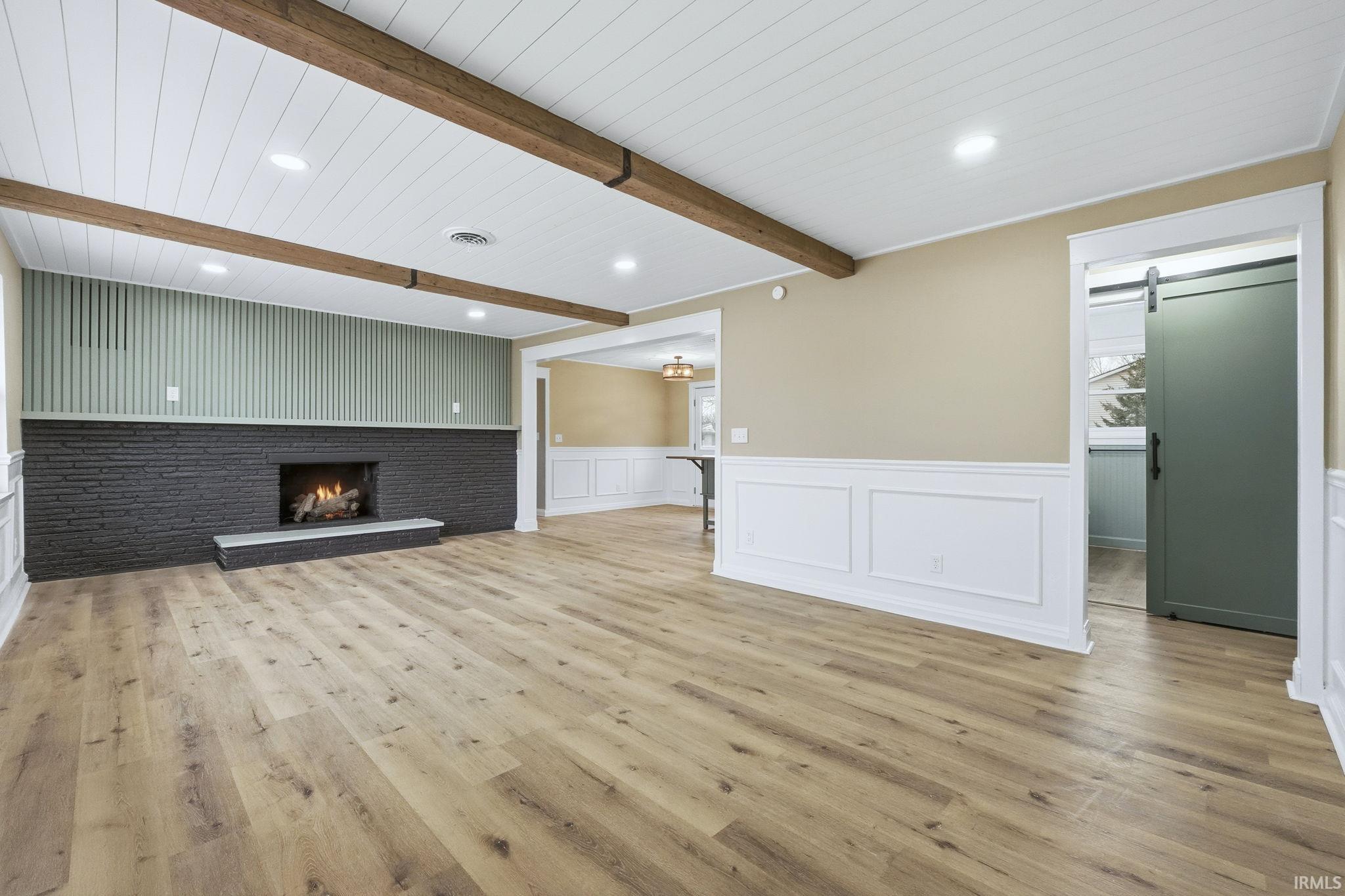 Unfurnished living room featuring a wainscoted wall, a decorative wall, light wood-style floors, a barn door, and a brick fireplace